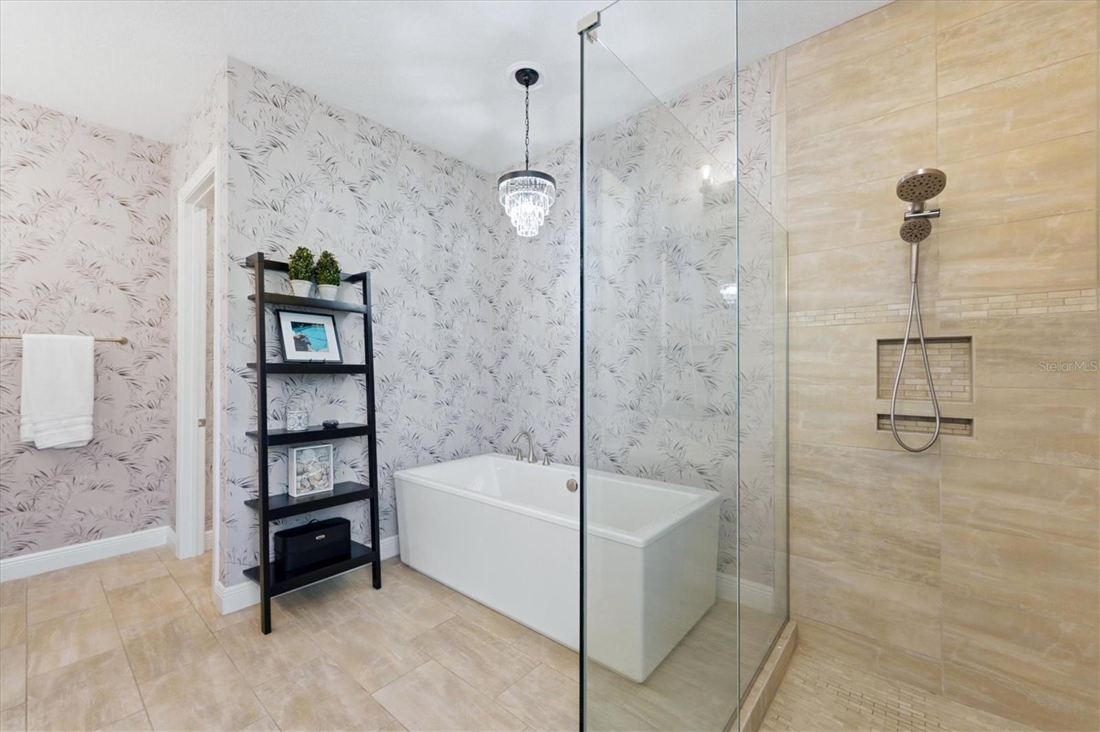 Bathroom with a freestanding tub, glass-enclosed shower, beige tile, and botanical wallpaper.