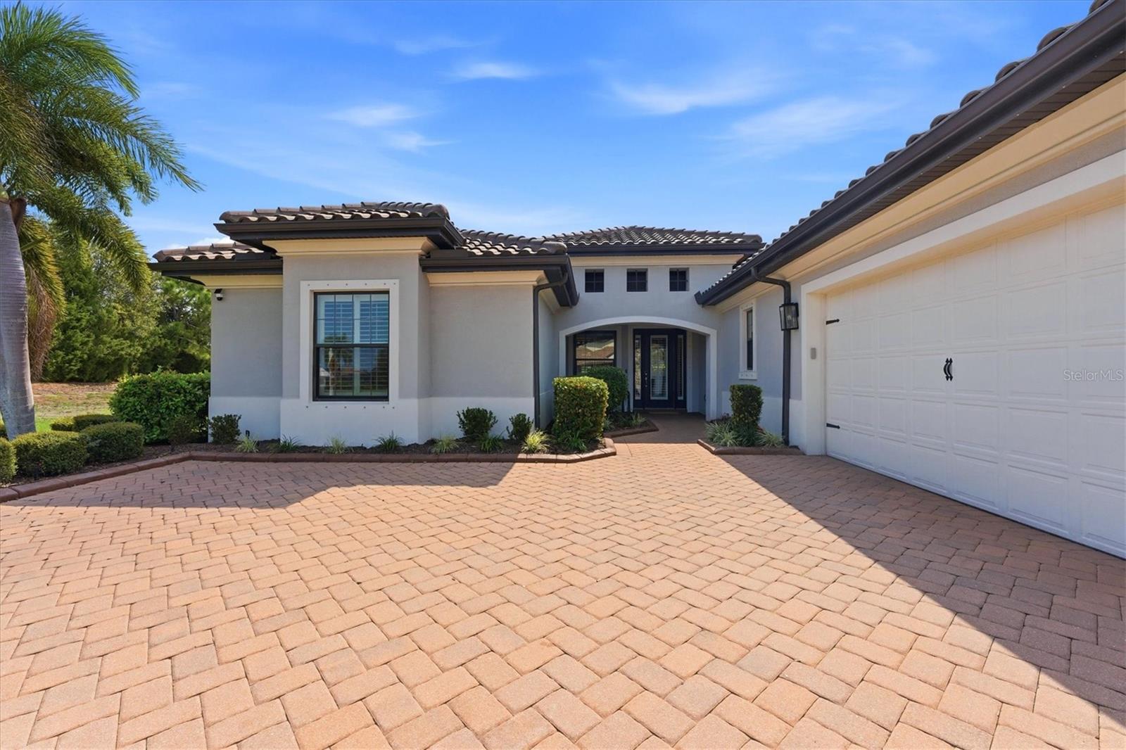 Home exterior with a wide paver driveway, tiled roof, and palm trees.