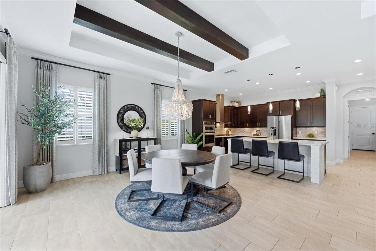 Open dining area and kitchen with dark wood cabinetry, ceiling beams, and a large island.