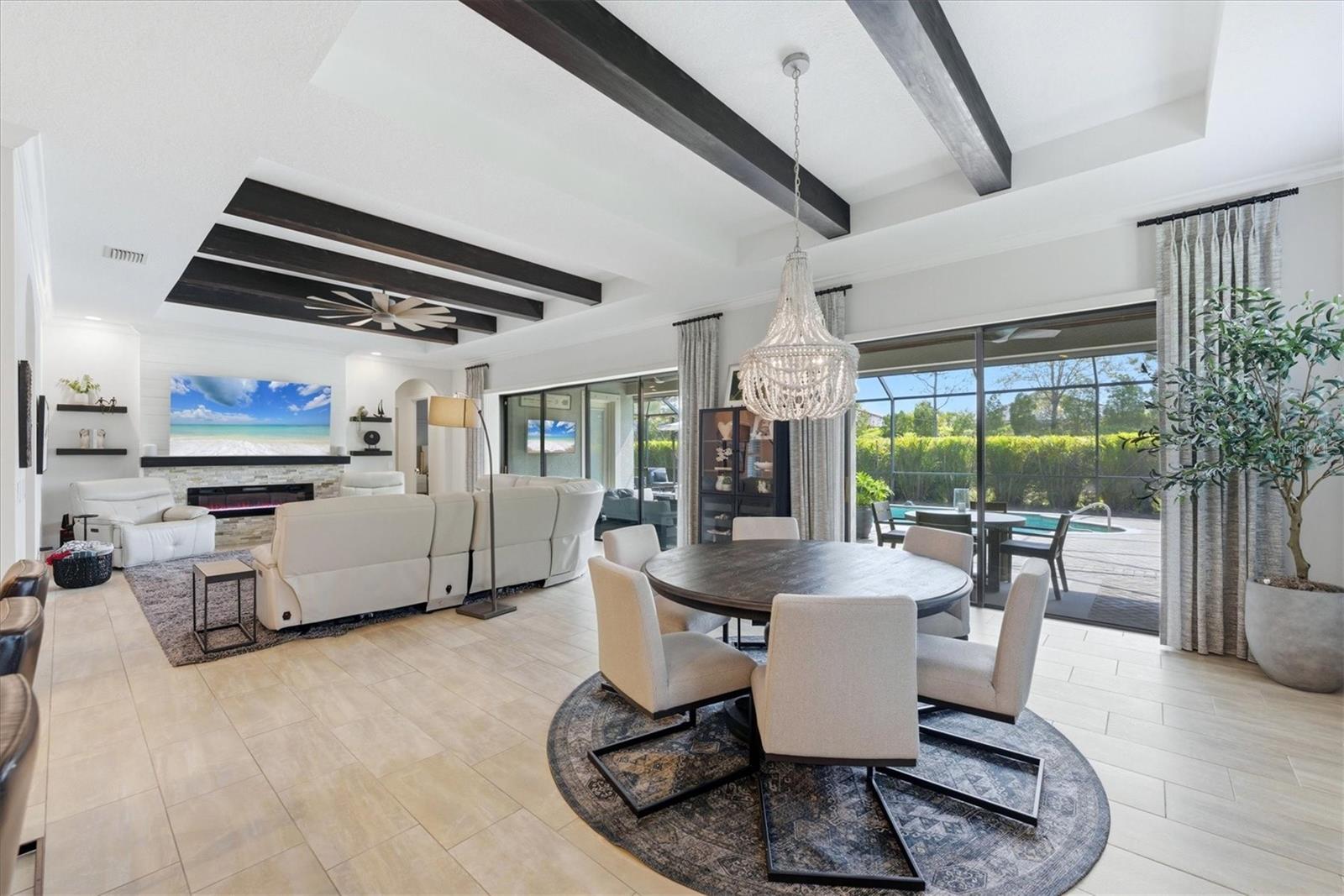 Open living and dining room with dark ceiling beams, a chandelier, and sliding doors to the pool patio.
