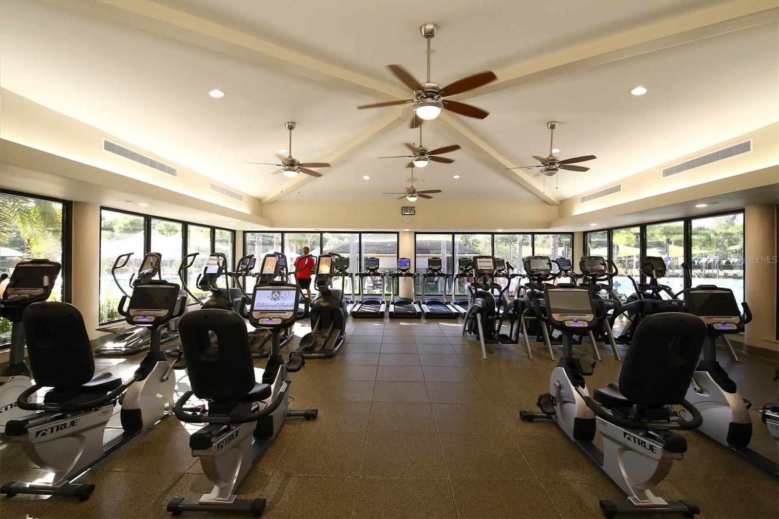 Community fitness center with cardio machines beneath a vaulted ceiling and broad windows.