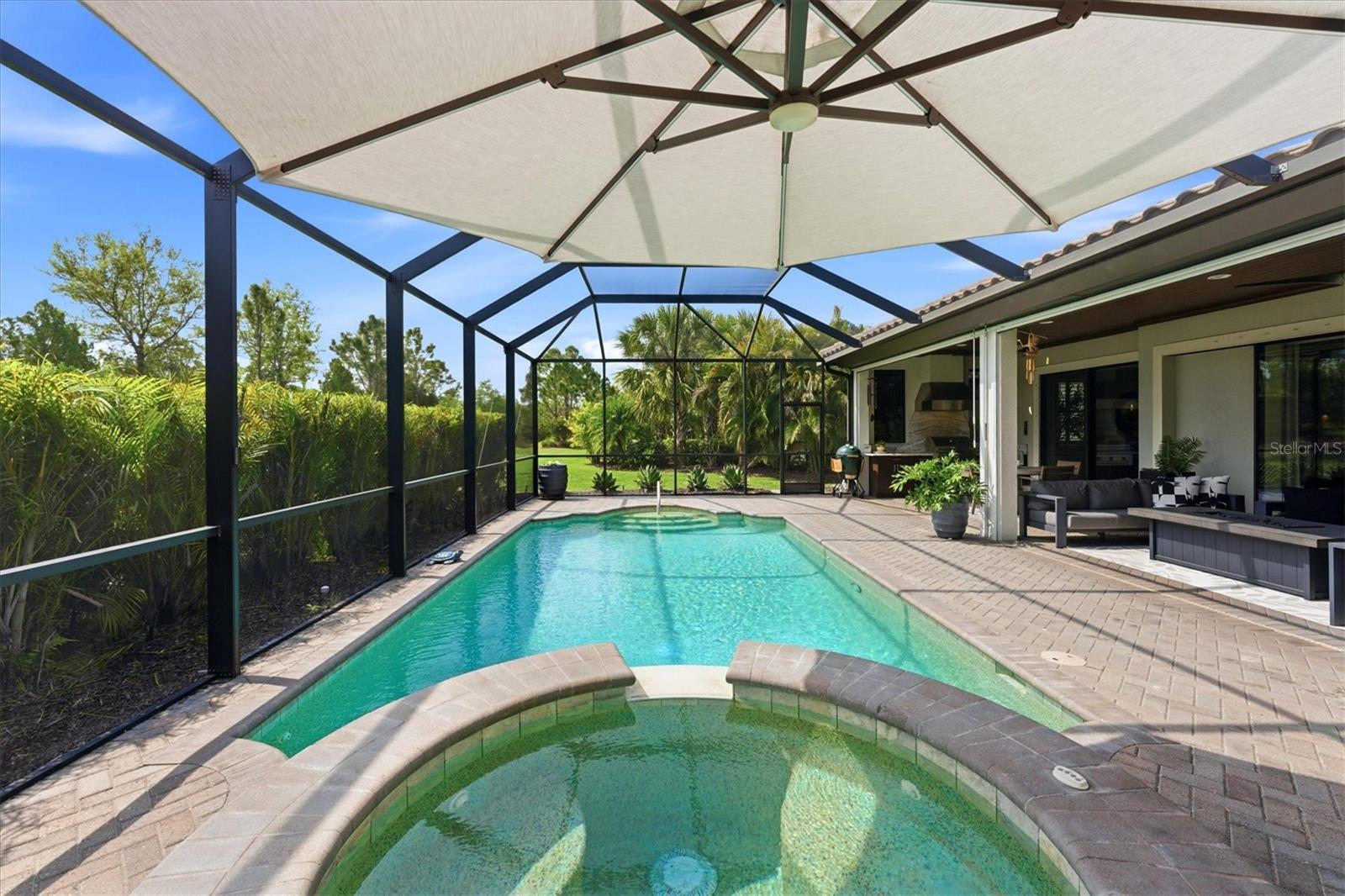 Screened backyard pool and spa beside a furnished covered patio.