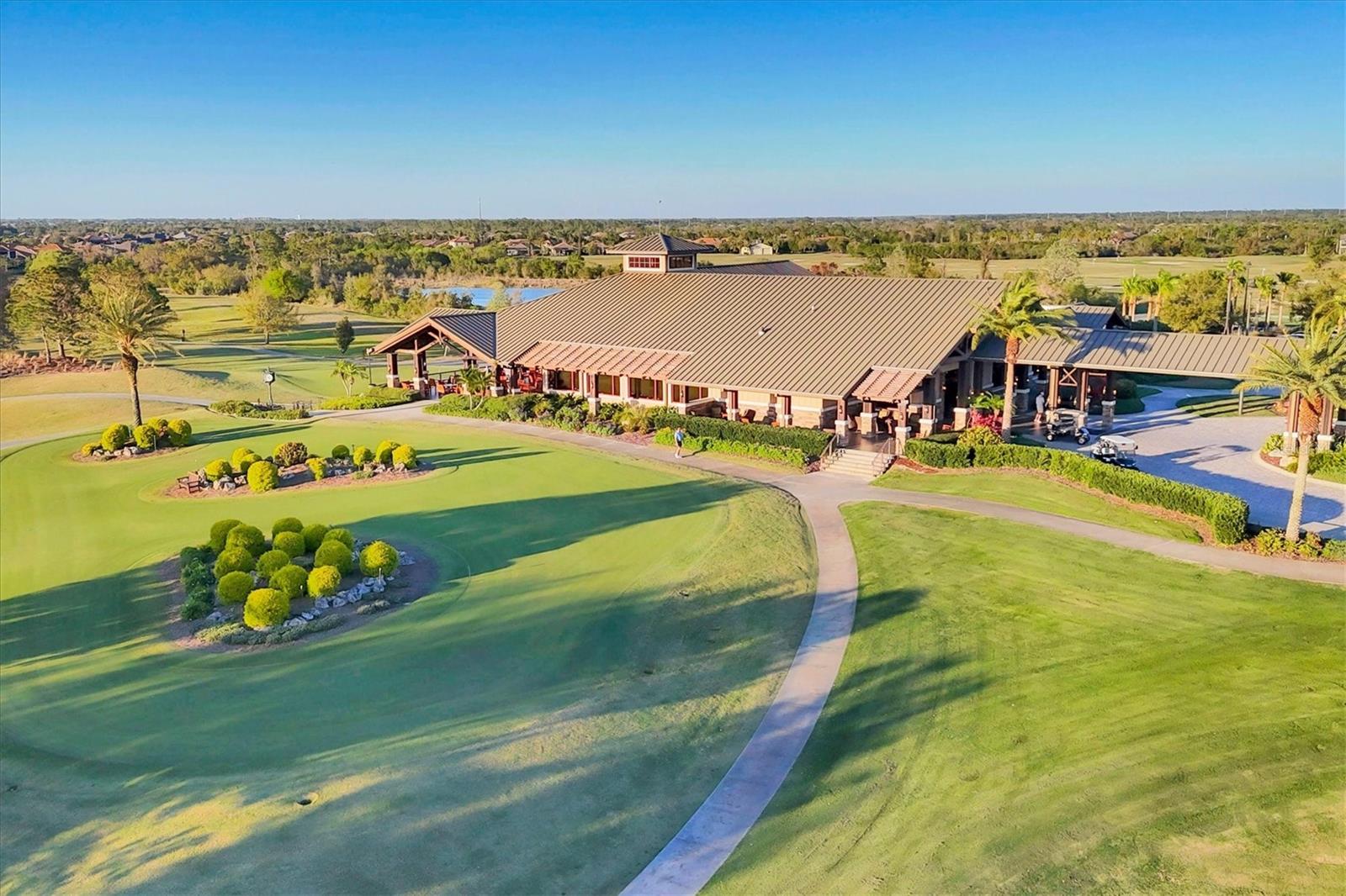 Aerial view of a golf clubhouse beside a putting green and curving cart path.