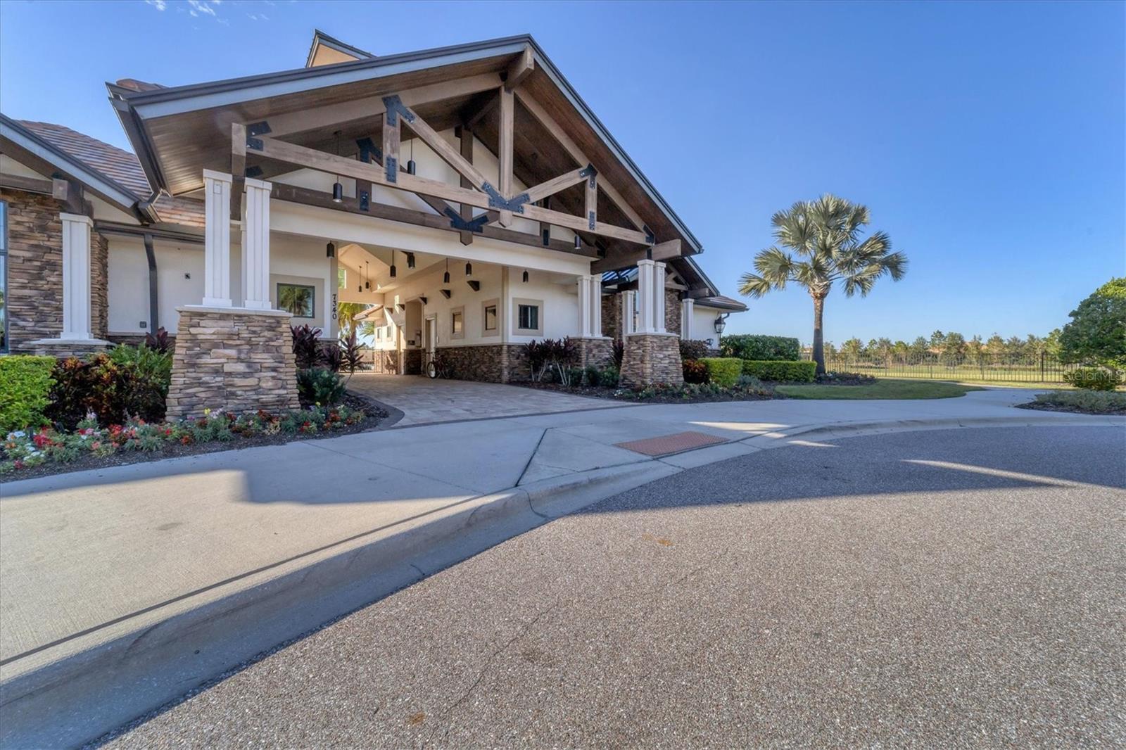 Covered entrance with timber trusses, stone columns, landscaped beds, and a palm tree.