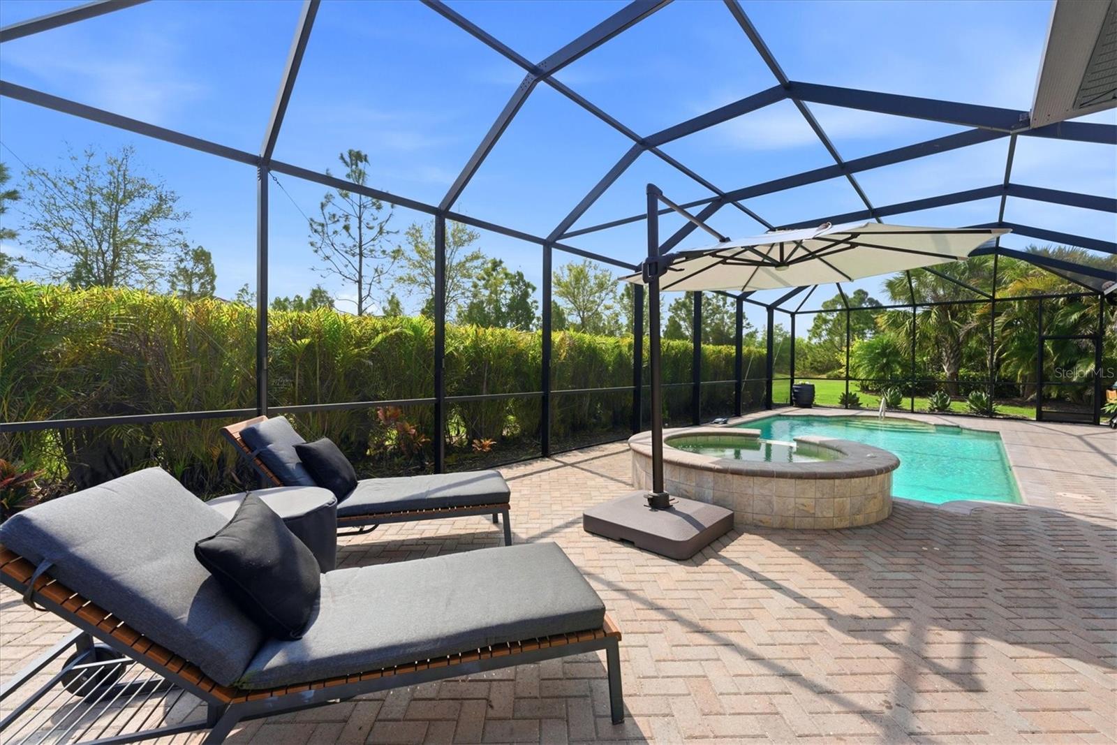 Screened pool patio with a raised spa, brick pavers, chaise lounges, and a shade umbrella.
