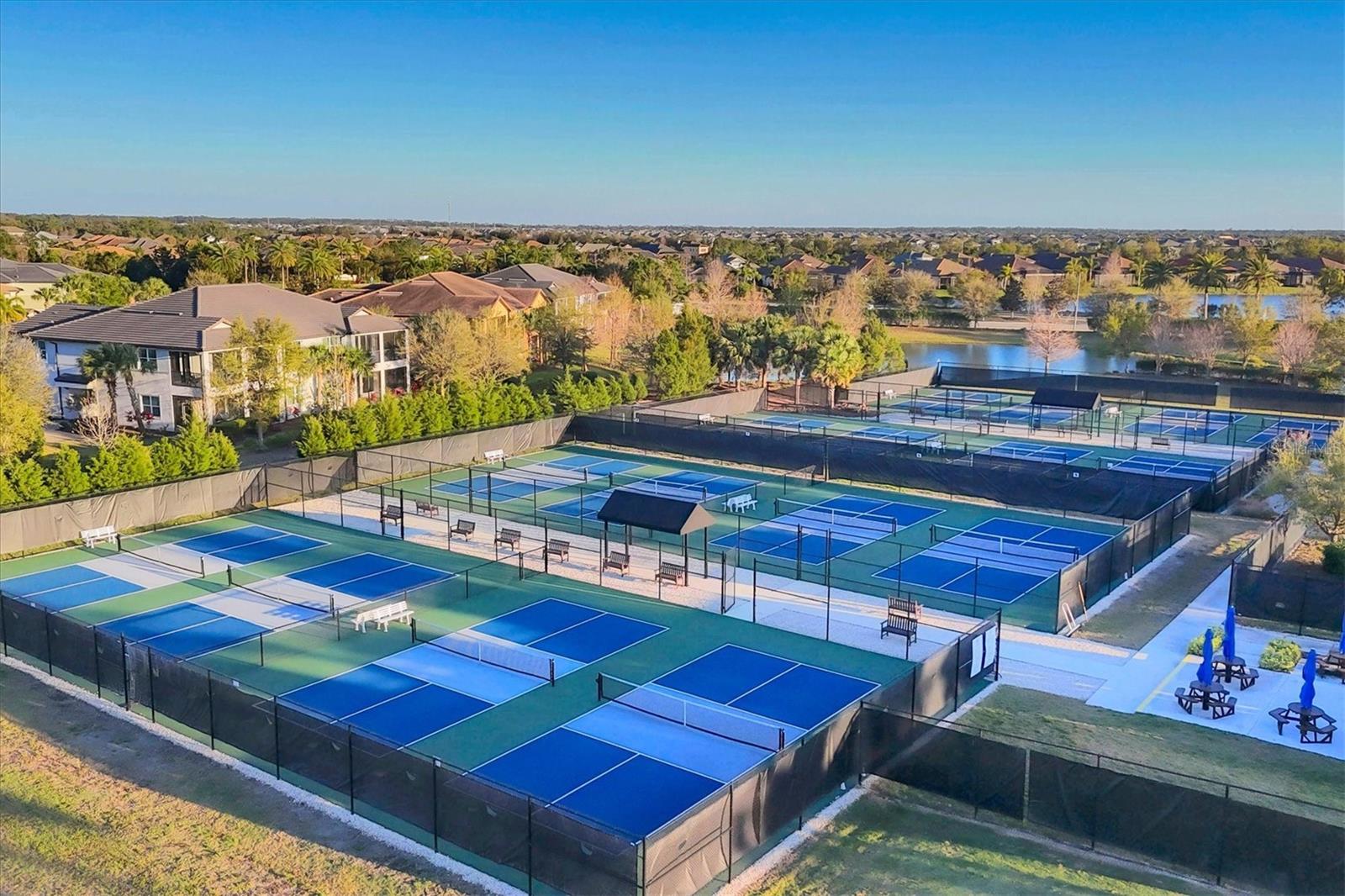 Aerial view of community pickleball courts beside a lake and surrounding homes.