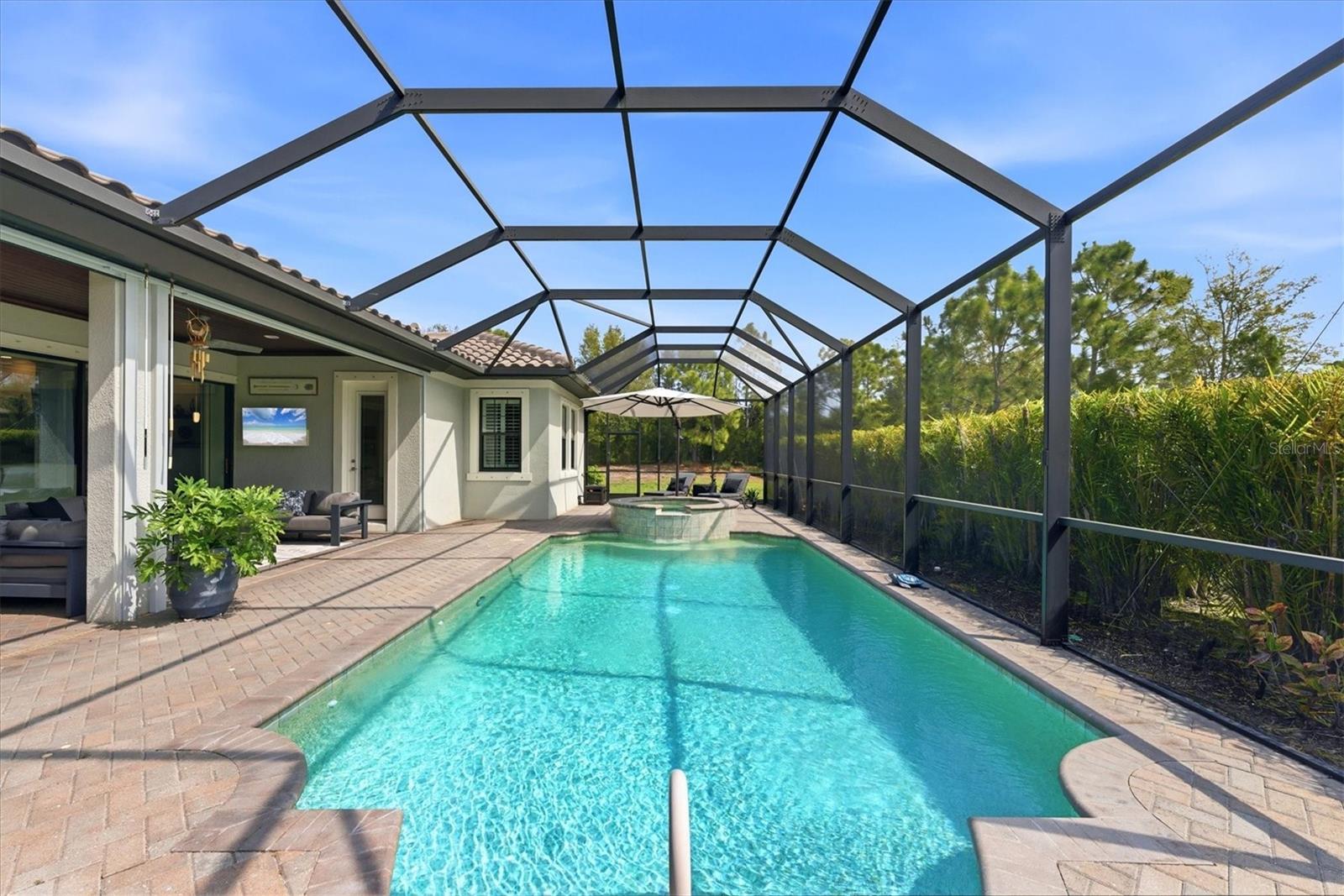 Backyard pool and attached spa beneath a screened lanai, with brick pavers and a covered seating area.