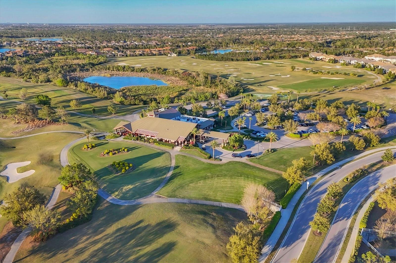 Aerial golf course with clubhouse, pond, fairways, and surrounding homes.