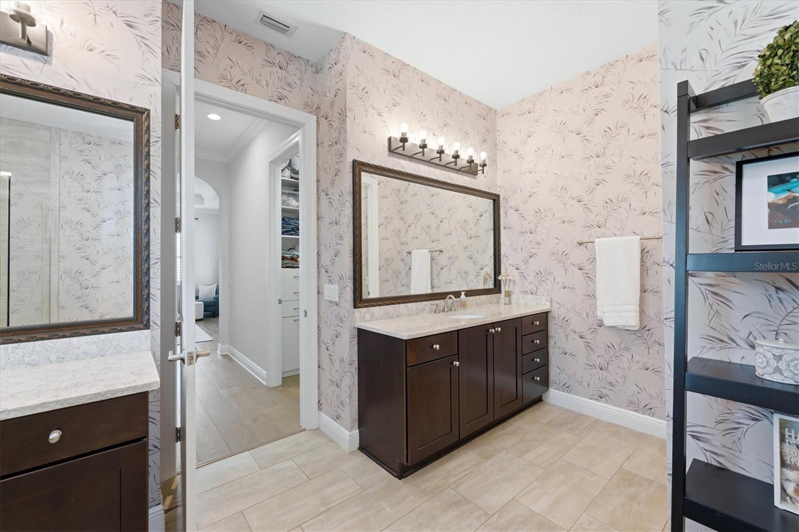 Bathroom with a dark wood double vanity, botanical wallpaper, and large framed mirrors.