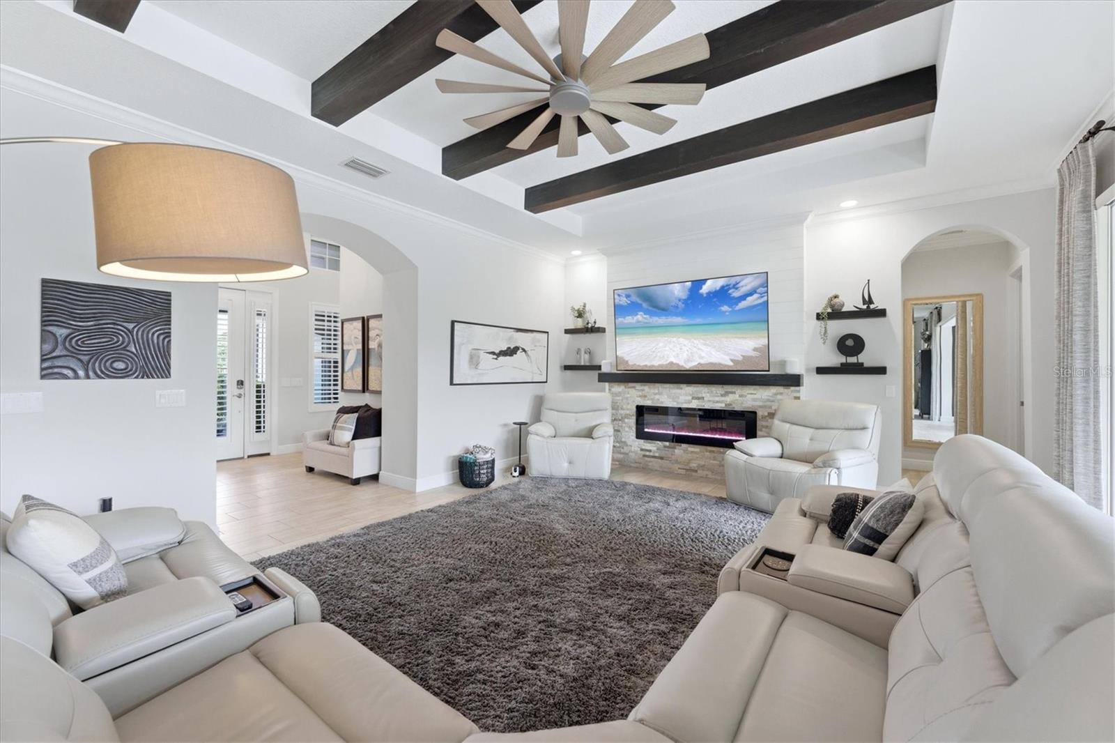 Living room with a stone fireplace, white leather seating, and dark ceiling beams.