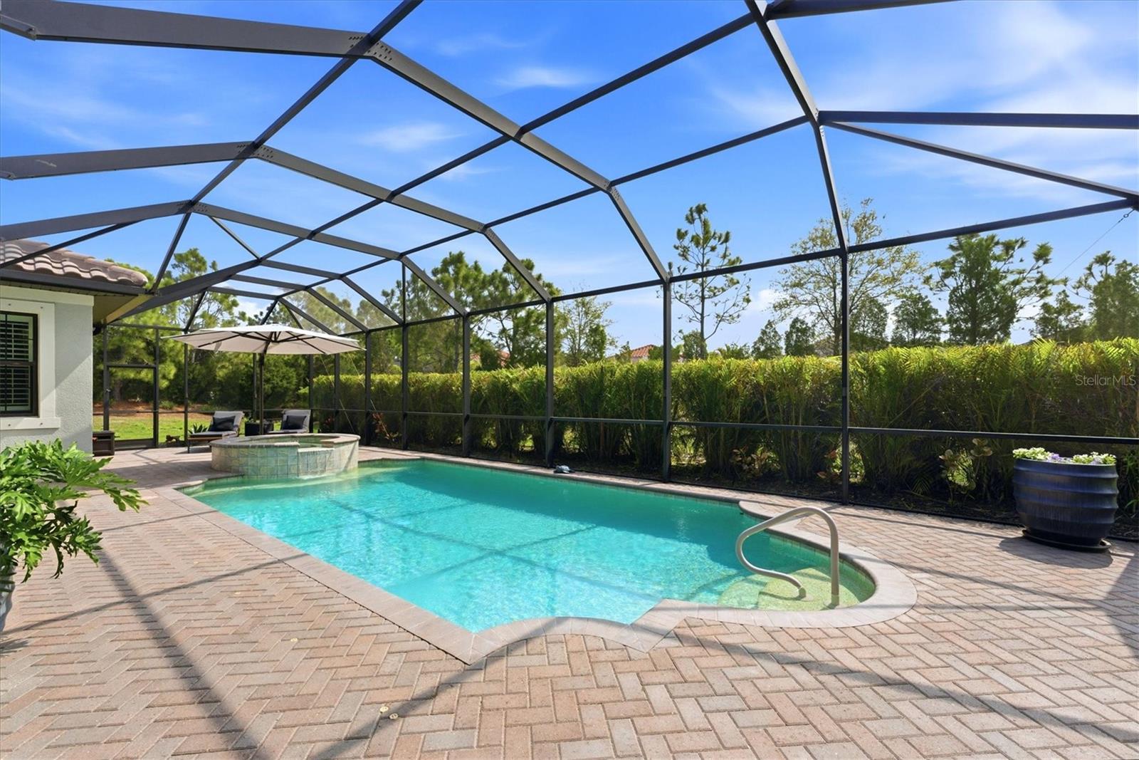 Screened pool and raised circular spa beside a brick paver patio and landscaped hedge.