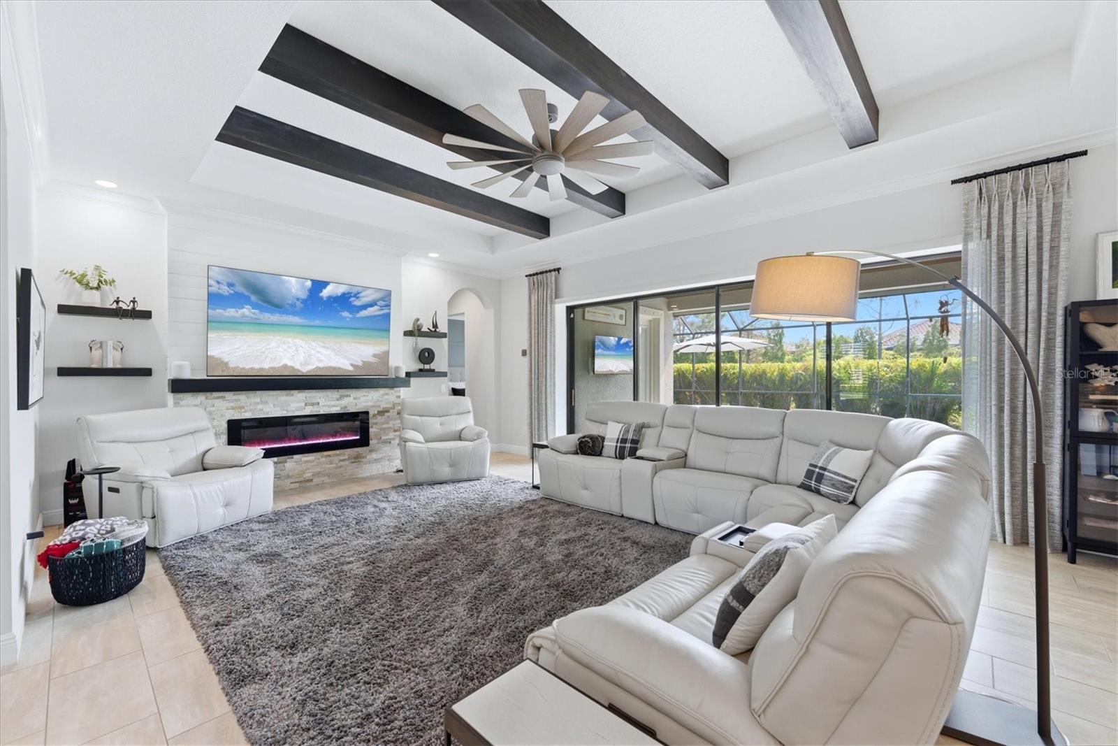 Living room with white reclining sofas, a stone fireplace, dark ceiling beams, and screened patio doors.