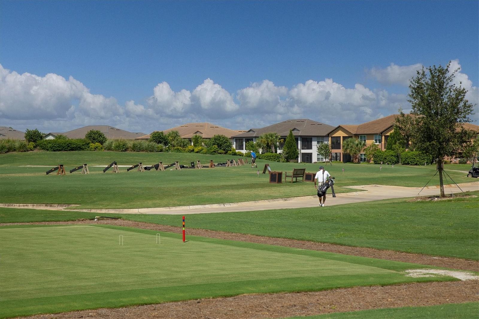 Golf practice green with golfers and homes bordering the course.