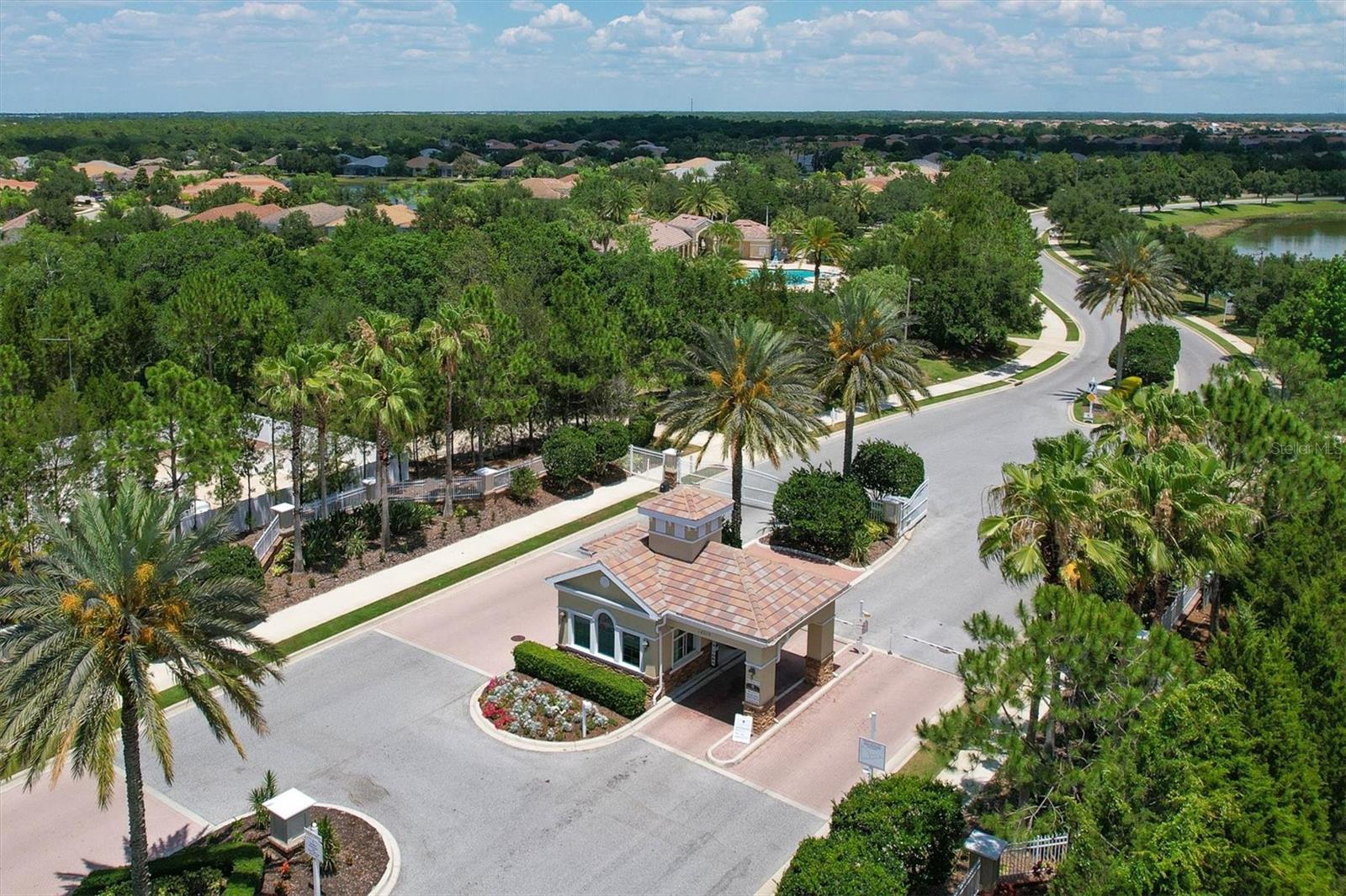 Aerial view of a landscaped neighborhood entrance with a tiled-roof gatehouse and curving road.