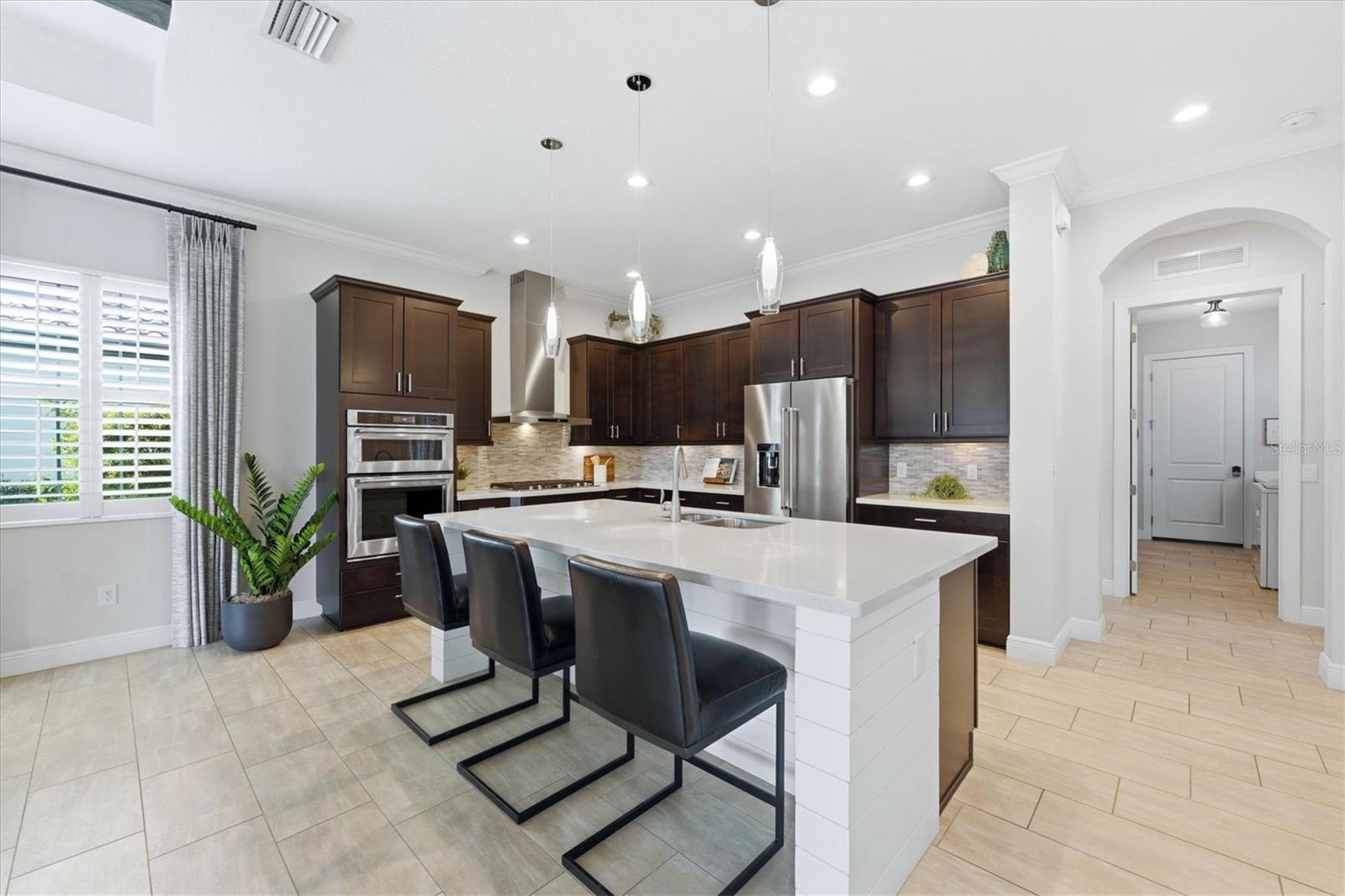 Modern kitchen with dark cabinetry, stainless steel appliances, and a large island with three bar stools.