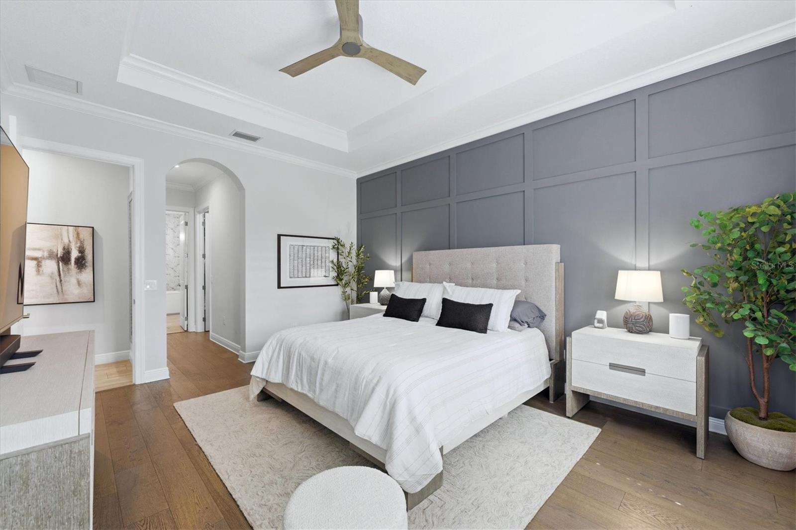 Bedroom with a king-size bed, gray paneled accent wall, and warm wood floors.