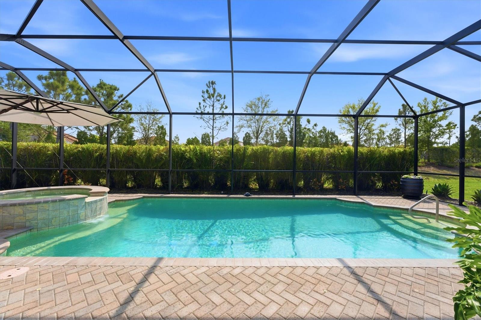 Backyard pool and raised spa beneath a screened lanai, with brick pavers and a shade umbrella.