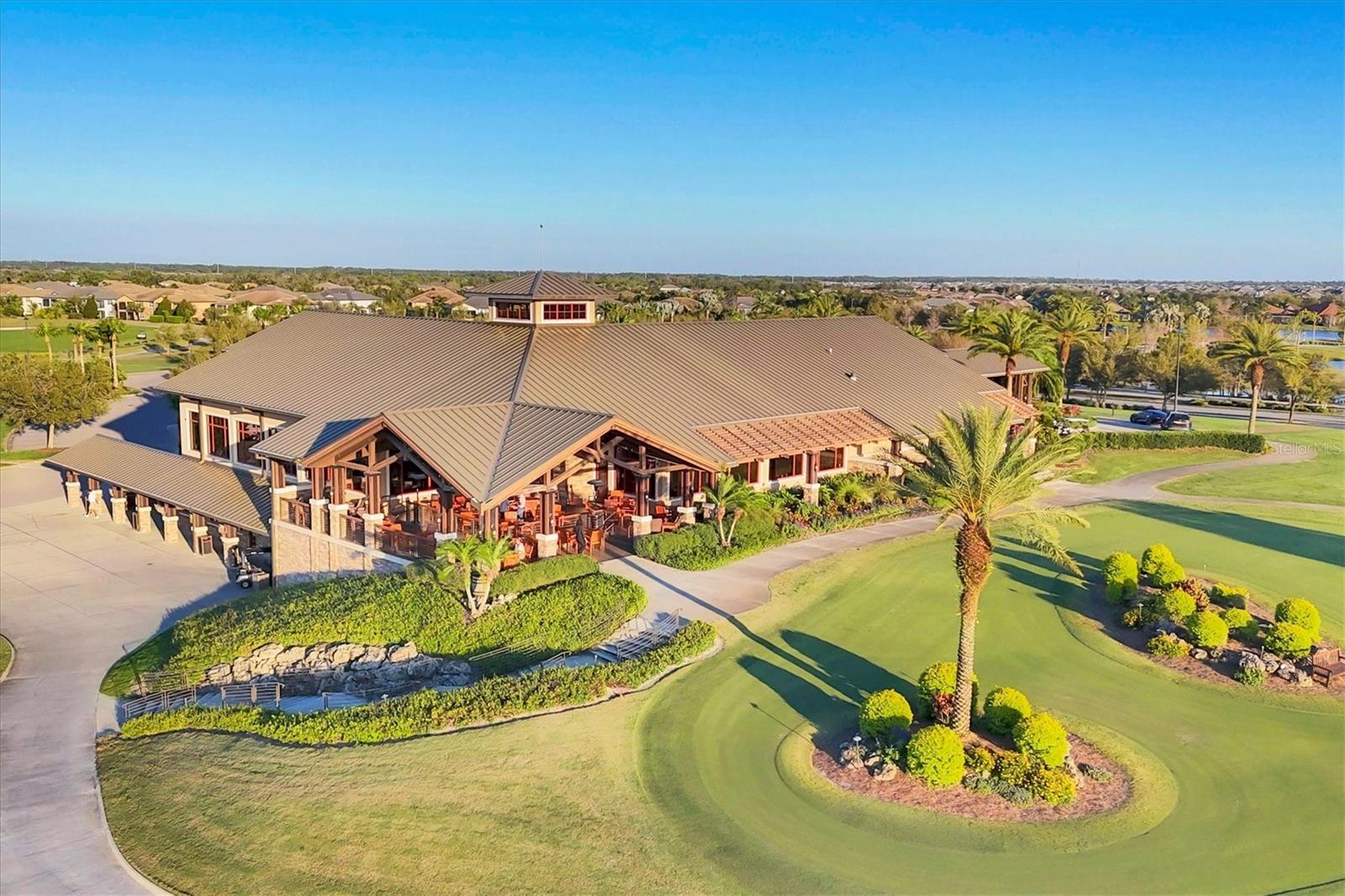 Aerial view of a clubhouse with a covered patio beside a landscaped putting green.