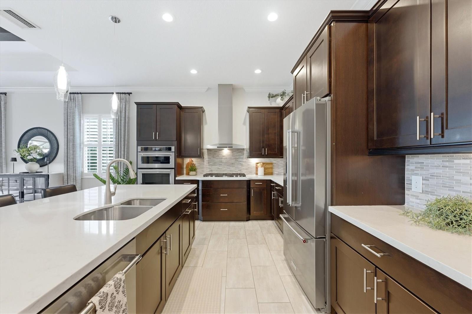 Kitchen with dark wood cabinets, a large white island, stainless steel appliances, and a mosaic backsplash.