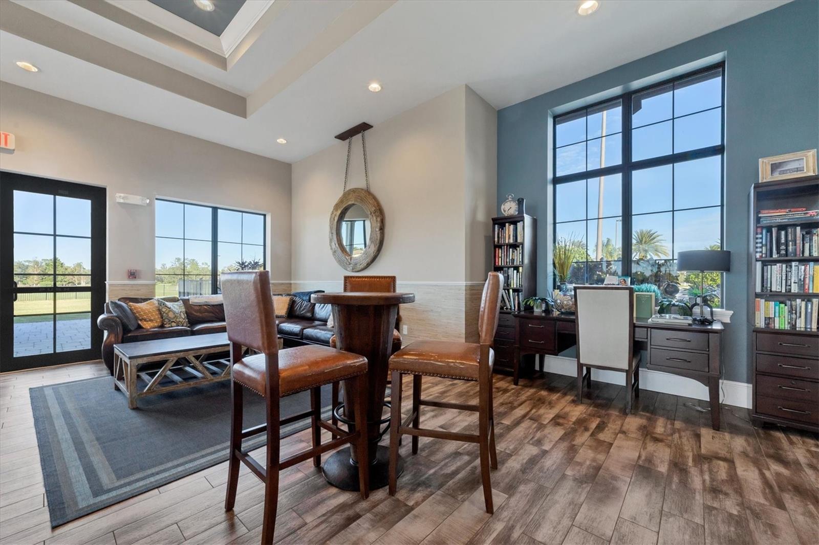 Living and dining area with a leather sectional, round table, tall windows, desk, and bookcases.