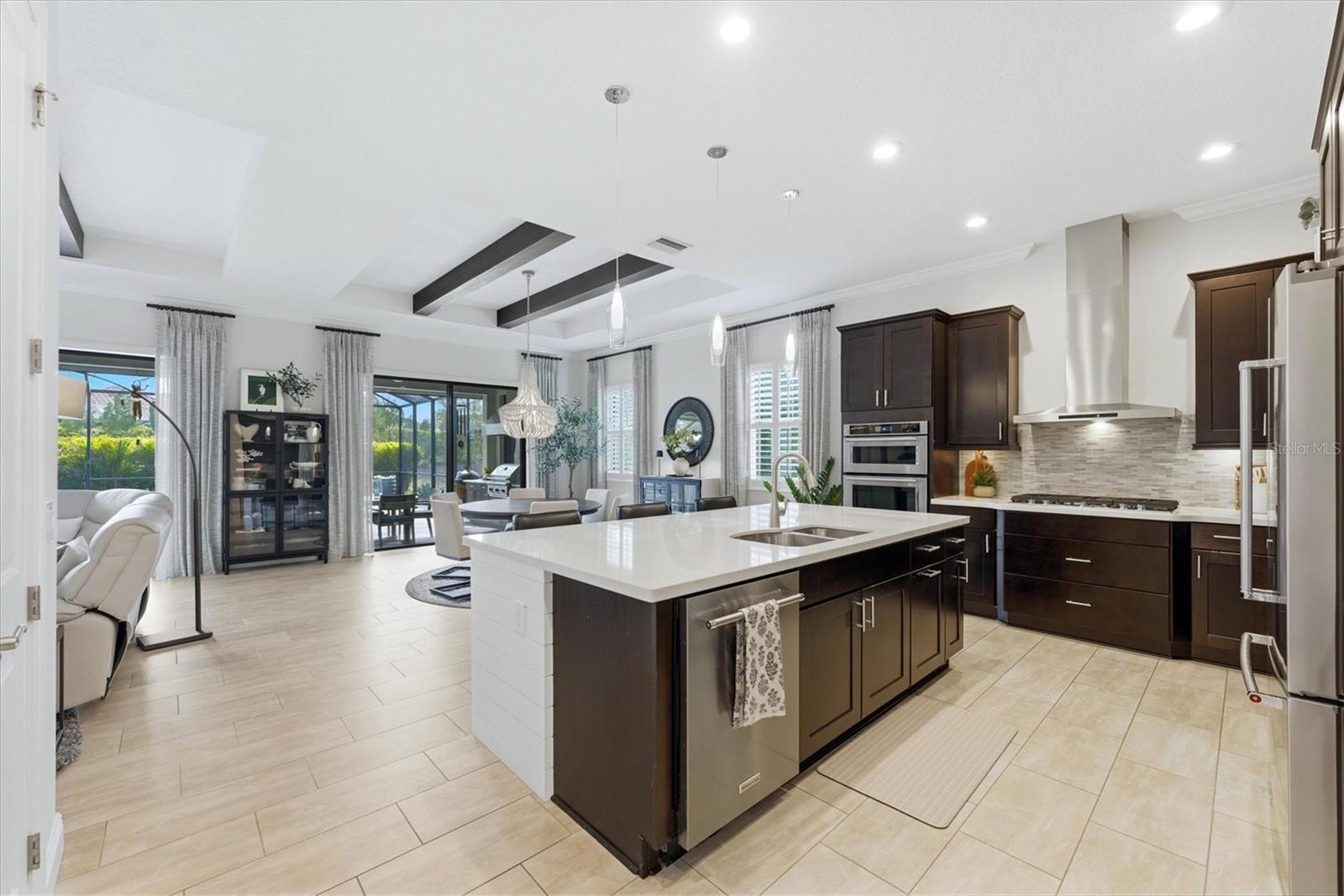 Open-plan kitchen with a large white island, dark cabinets, stainless steel appliances, and sliding glass doors.