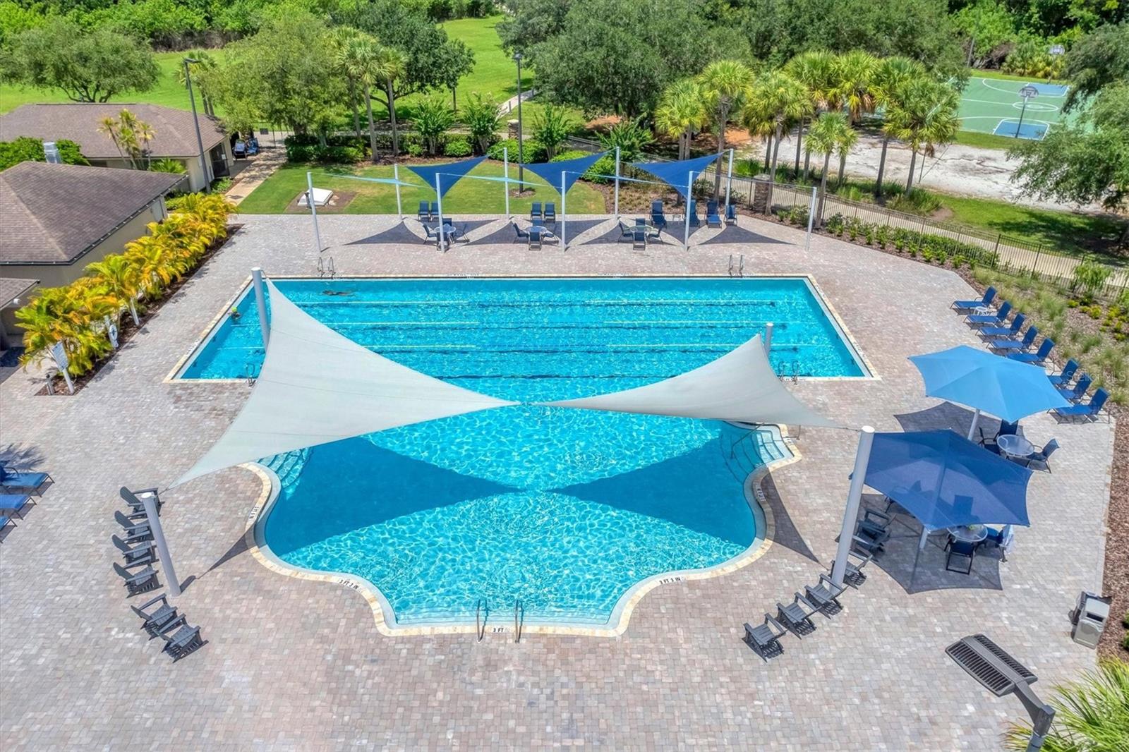 Community swimming pool with shade sails, lounge chairs, and a sports court nearby.