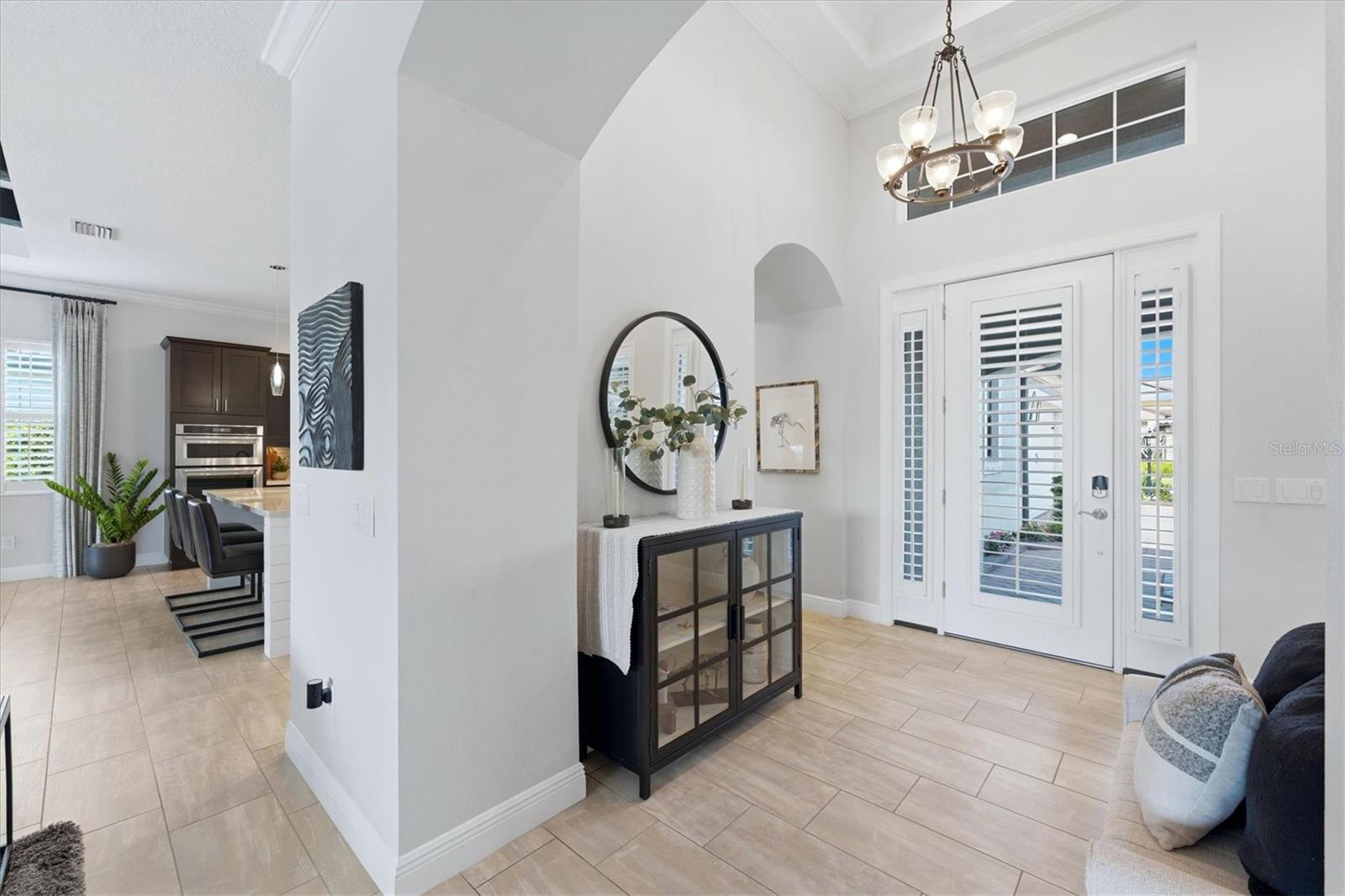 Entry foyer with vaulted ceiling, tiled floor, chandelier, and shuttered front door.