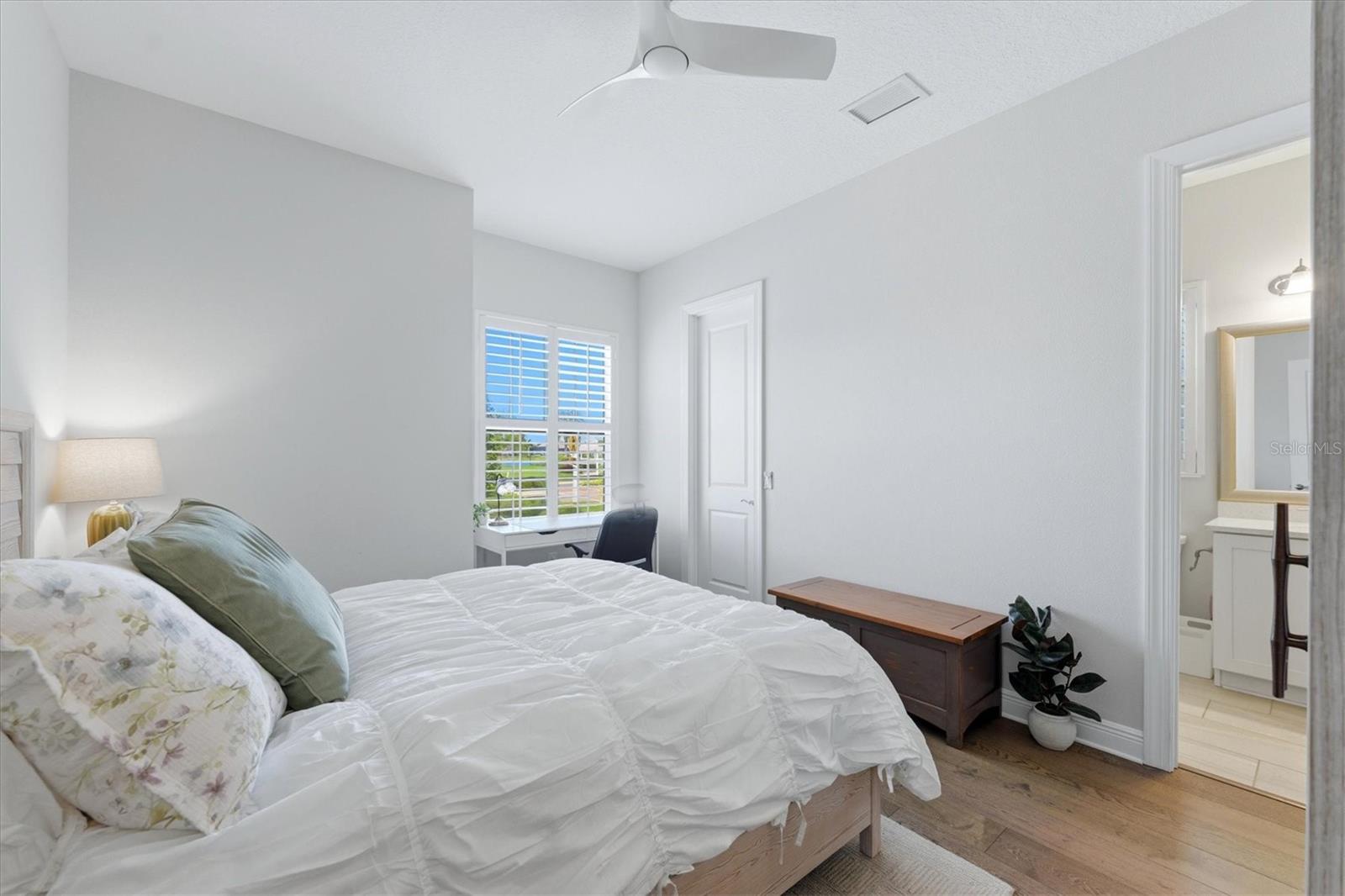 Furnished bedroom with a white bed, shuttered window, and doorway to an en suite bathroom.