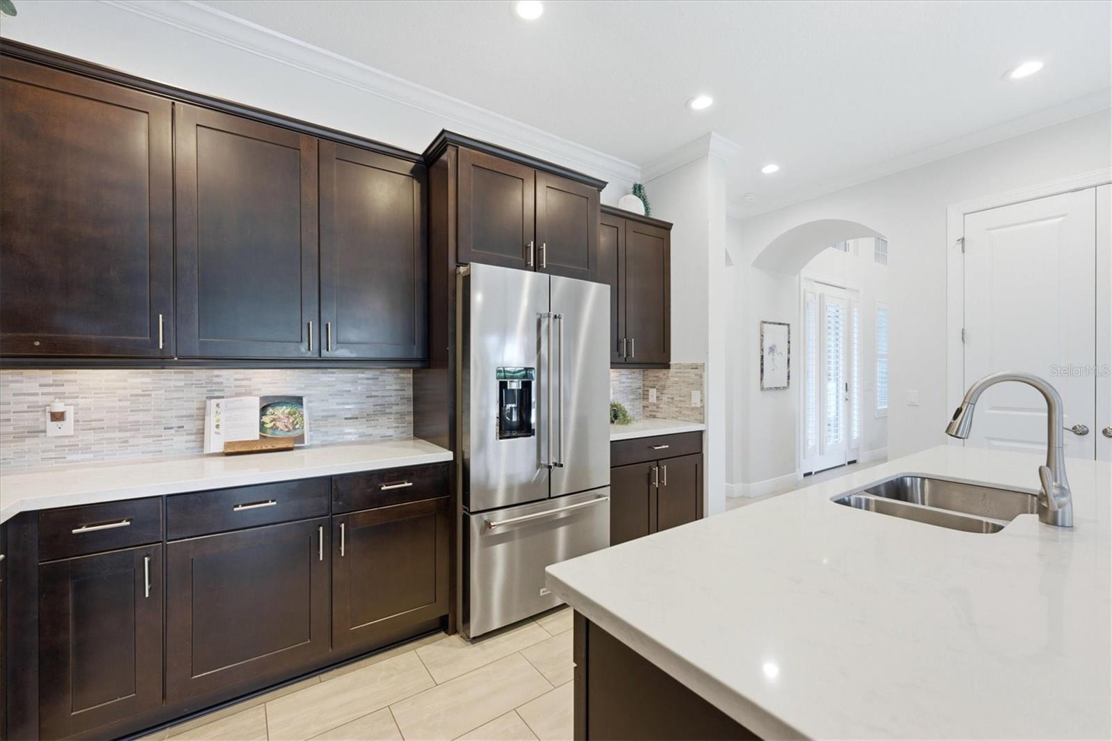 Kitchen with dark wood cabinets, stainless steel refrigerator, and a white island with a double-basin sink.