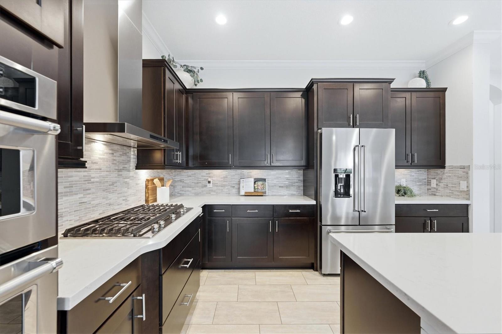 Kitchen with dark wood cabinetry, stainless steel appliances, gas cooktop, and white countertops.