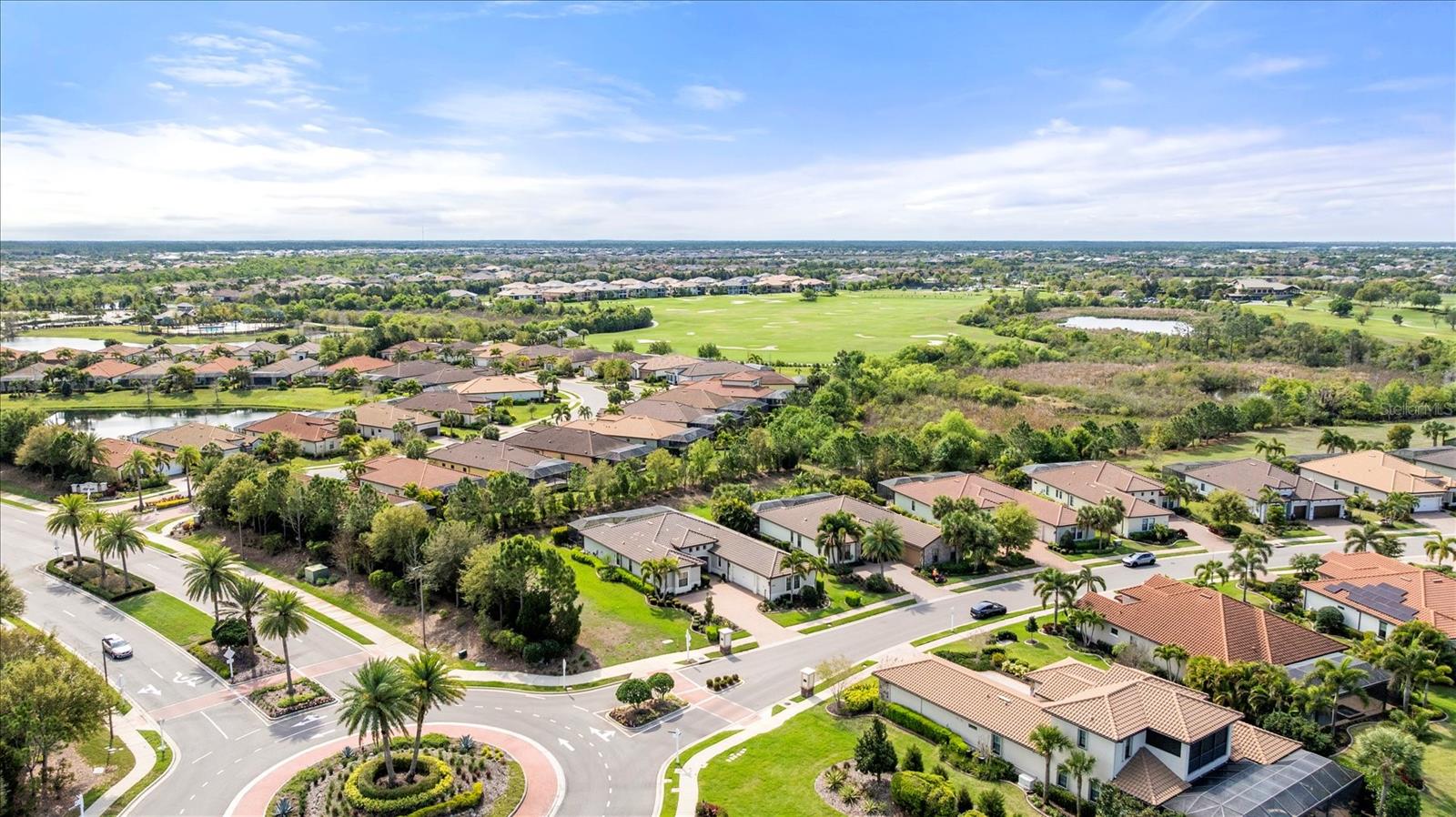 Aerial view of homes and palm-lined streets beside a golf course and ponds.