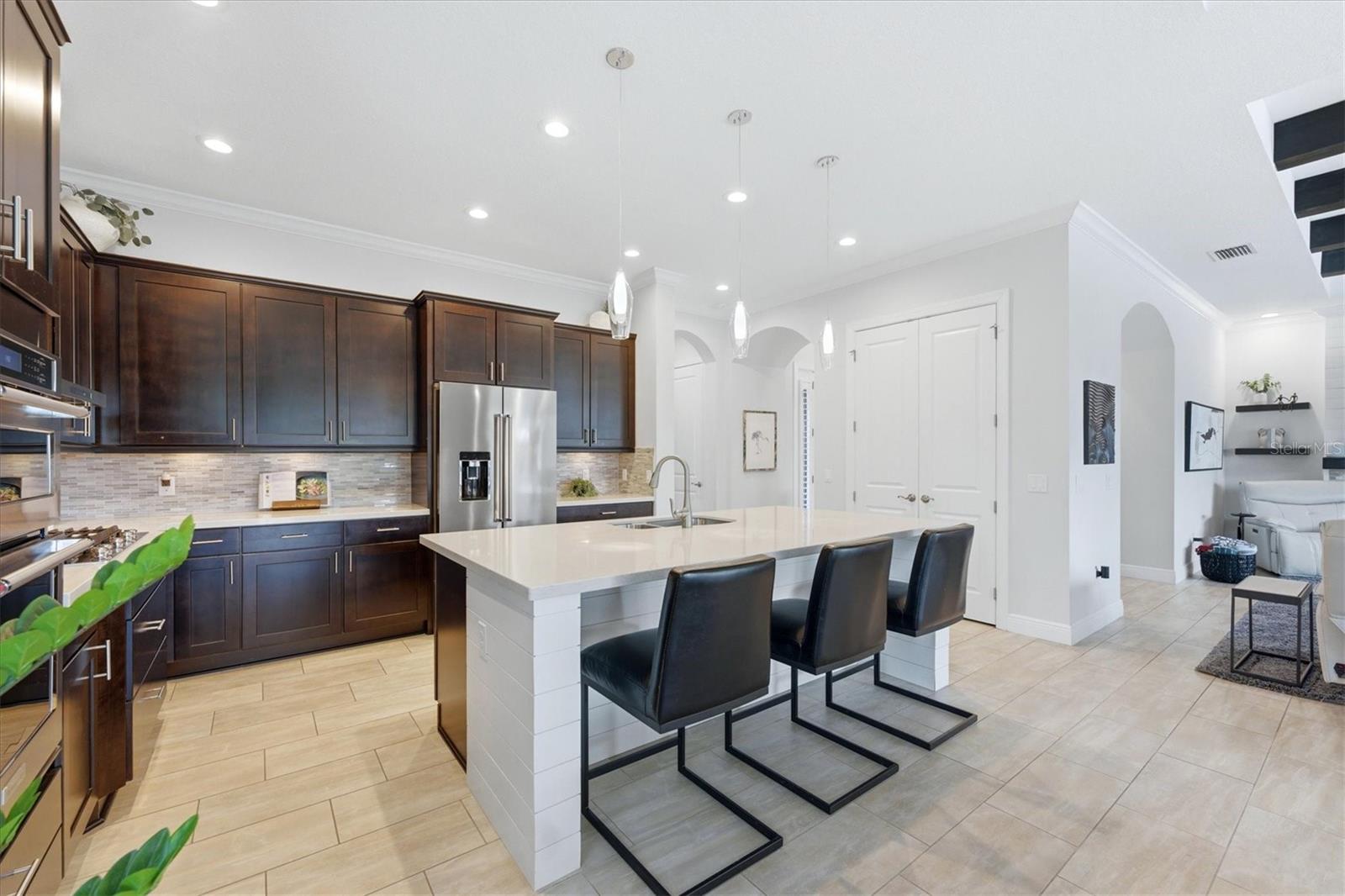 Kitchen with dark wood cabinets, stainless steel appliances, and a large white island with black bar stools.