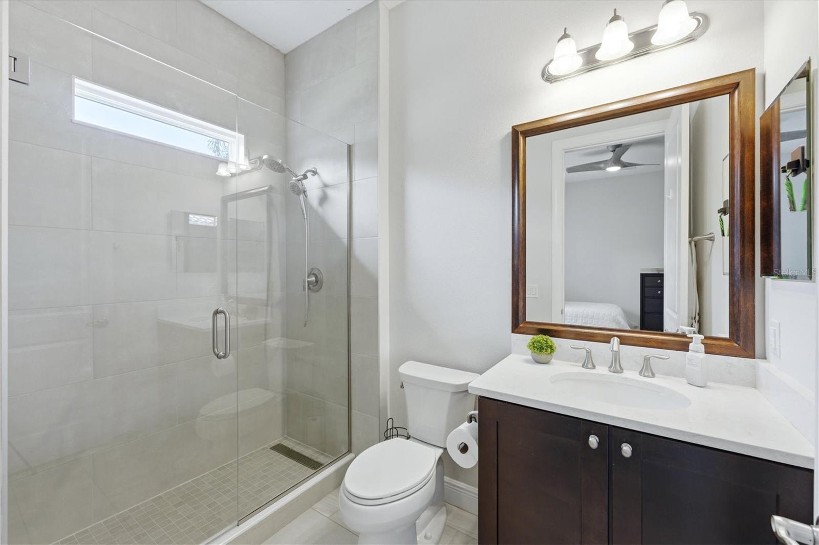 Bathroom with a glass-enclosed tiled shower, dark wood vanity, and large framed mirror.