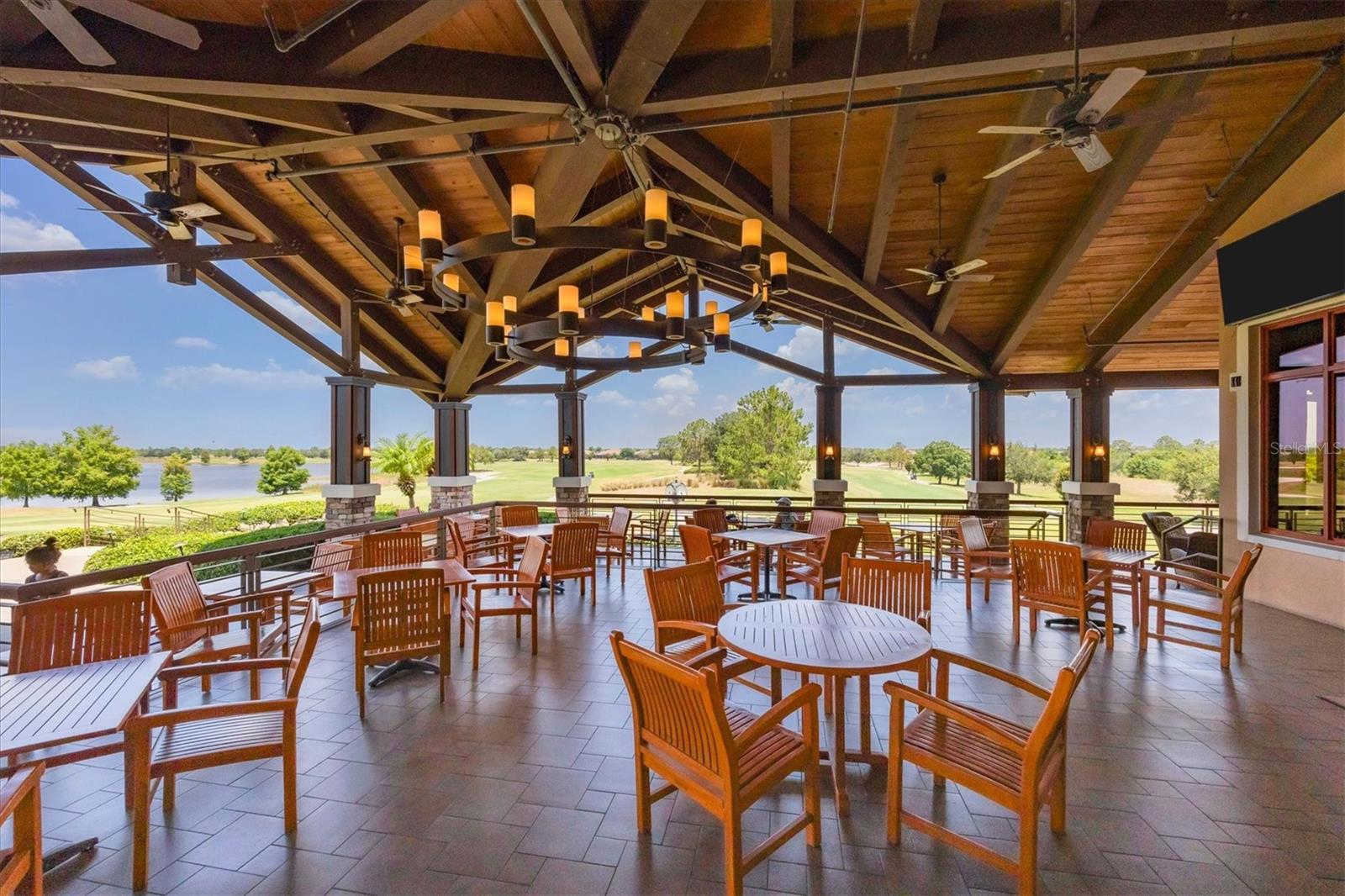 Covered patio with wooden dining furniture overlooking a lake and golf course.