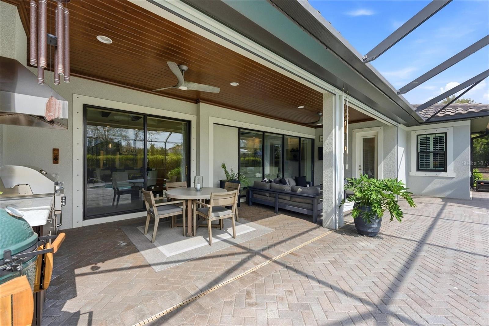 Covered patio with wood ceiling, dining set, lounge seating, and grill beside the house.