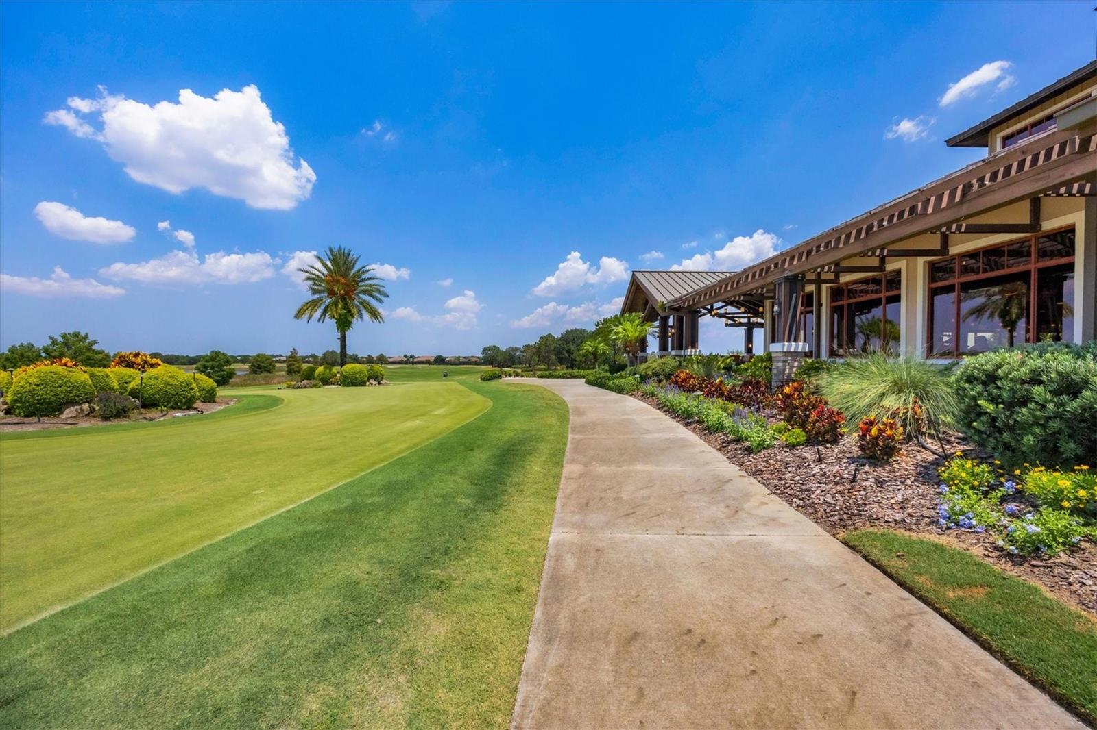 Golf course grounds and clubhouse beside a landscaped walkway.