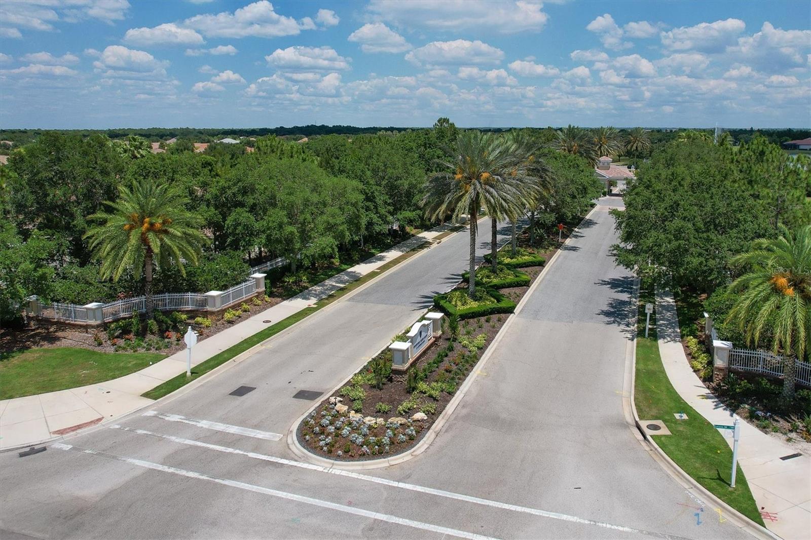 Aerial view of a residential entrance road with palm trees and a landscaped median.