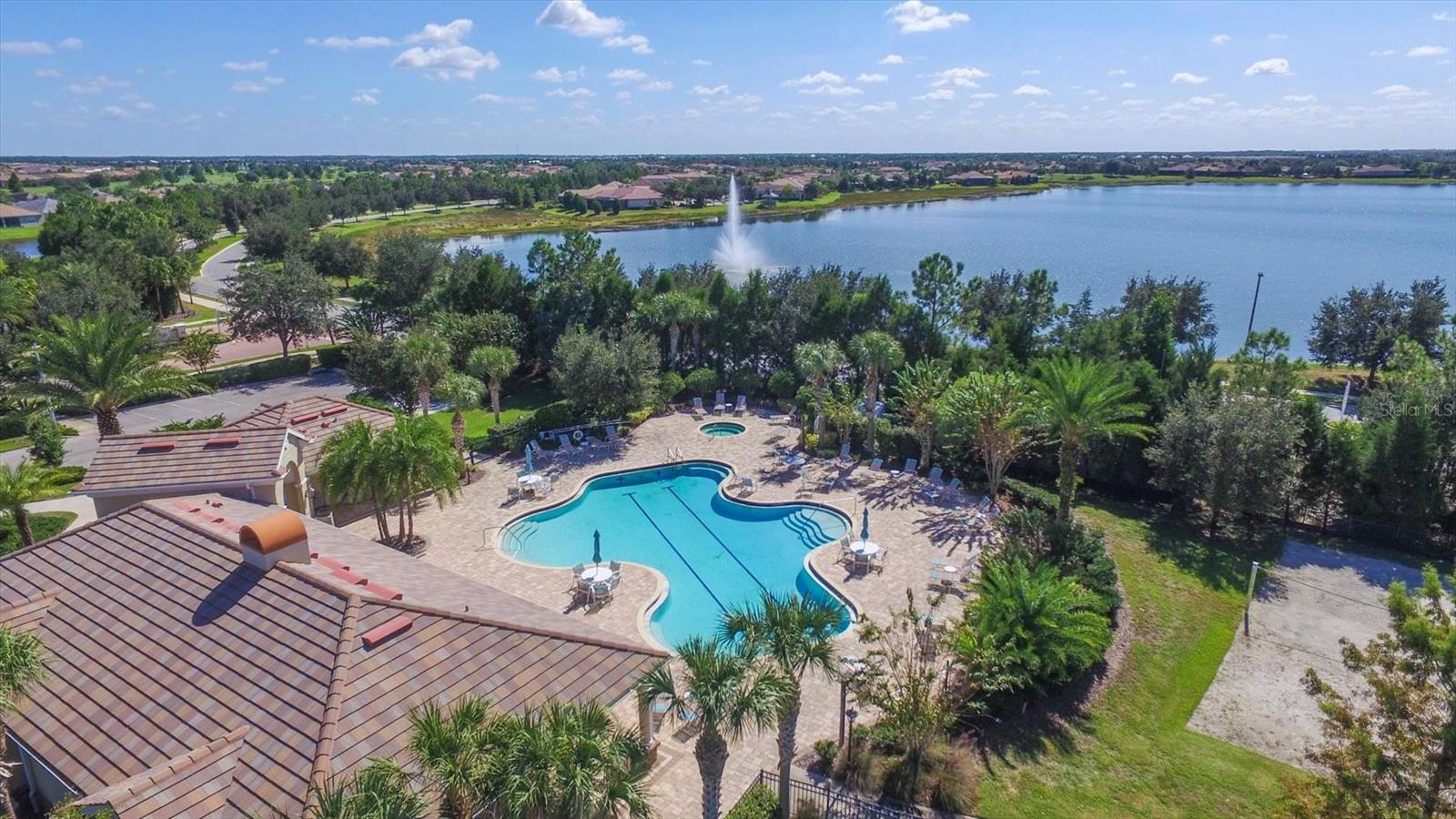 Aerial view of a curving community pool beside a lake with a fountain.