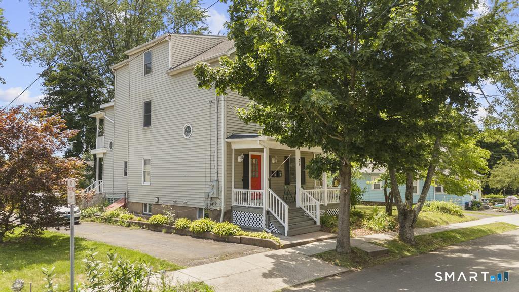 Multi-story house with a red front door, white porch railings, and mature street trees.