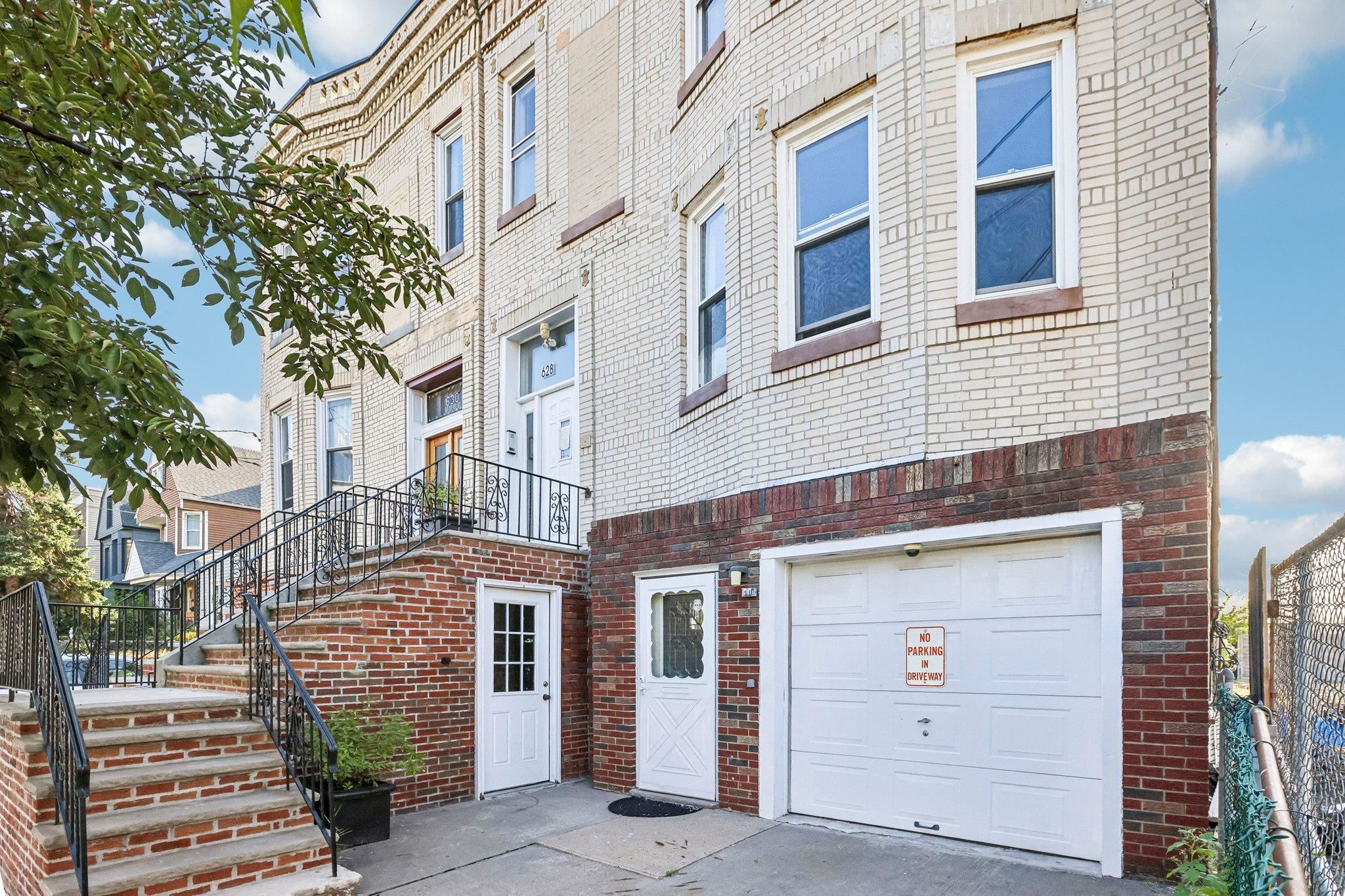 Multi-unit brick building with front stairs, separate entrances, and a white garage door.