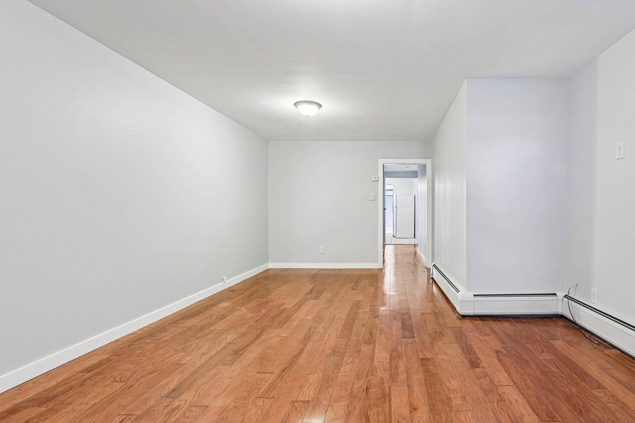 Empty room with hardwood floors, white walls, and a doorway to an adjoining space.
