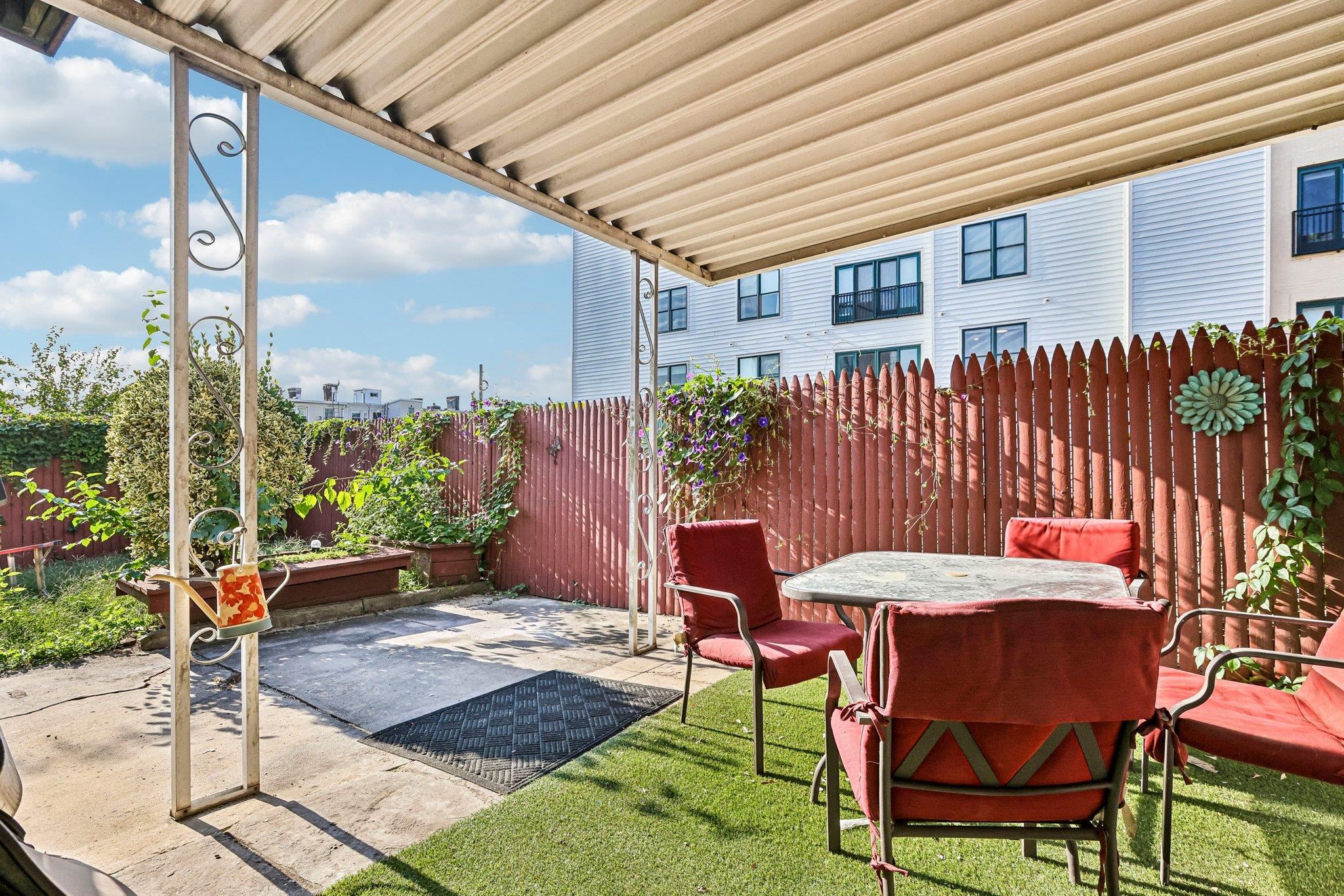 Covered patio with red seating, a round table, raised flower beds, and a red privacy fence.