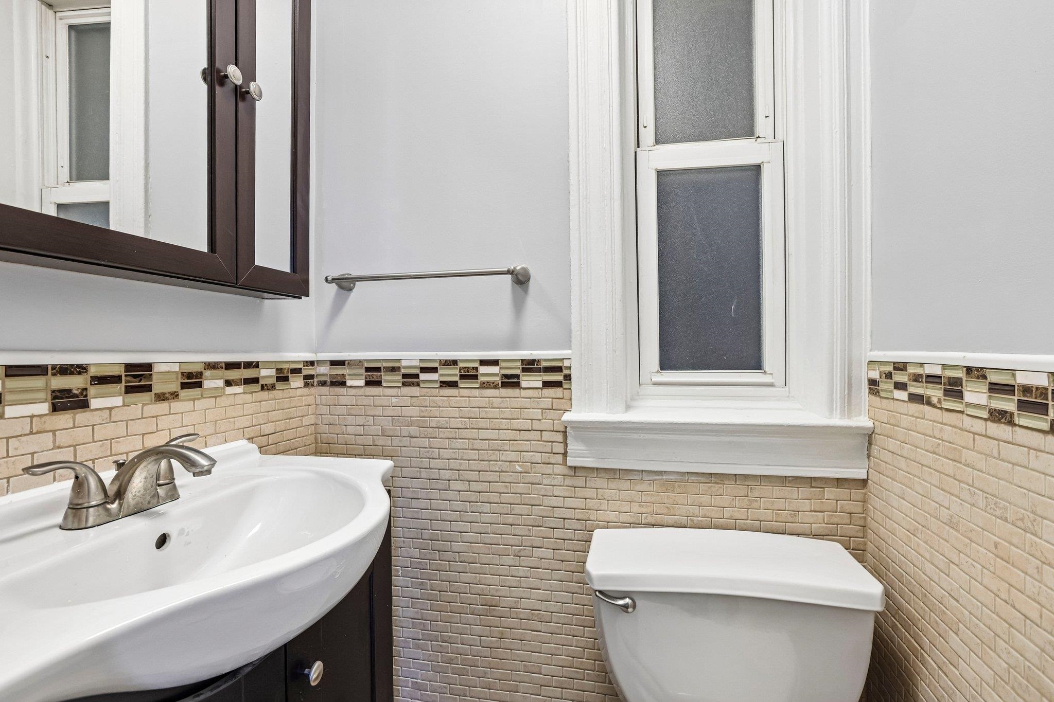 Bathroom with a white sink and toilet, frosted window, and beige tile walls.