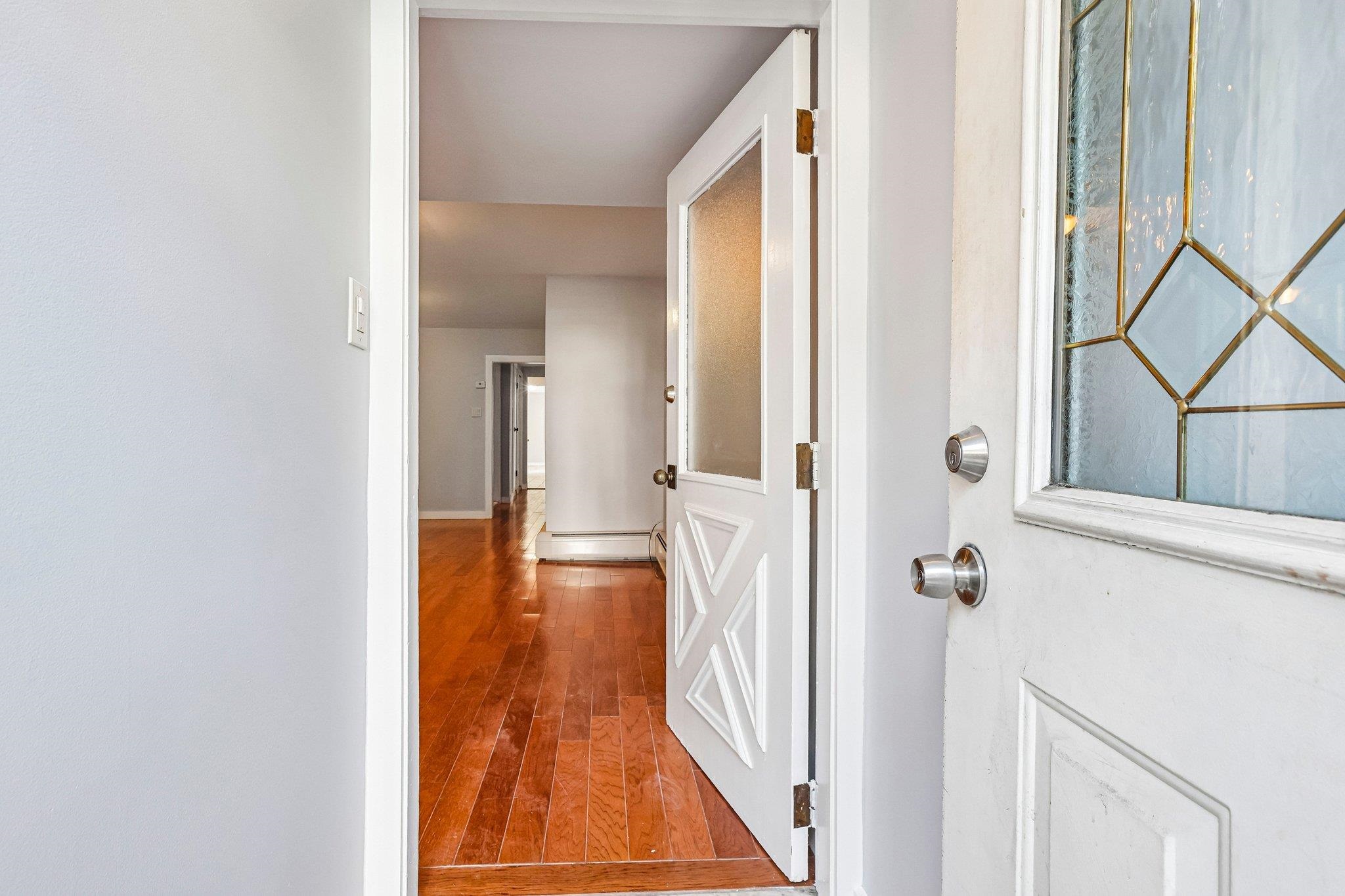 Open front door leading into a vacant entry hall with reddish hardwood floors and a decorative glass sidelight.