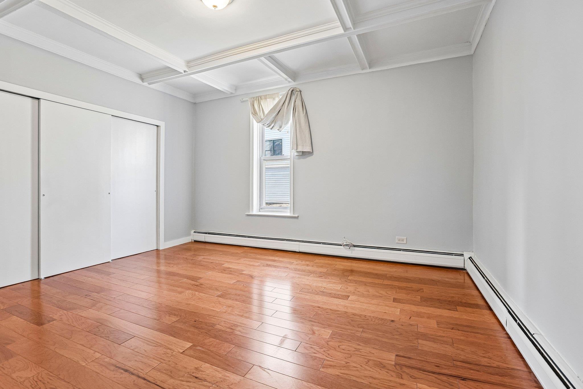 Empty bedroom with hardwood floors, a coffered ceiling, and a sliding-door closet.