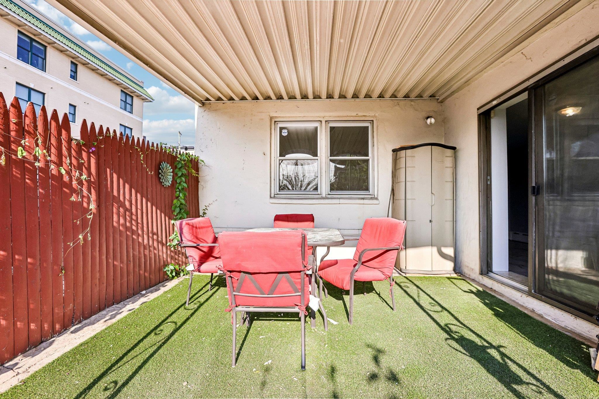 Covered patio with artificial turf, red fence, and red chairs around a table.