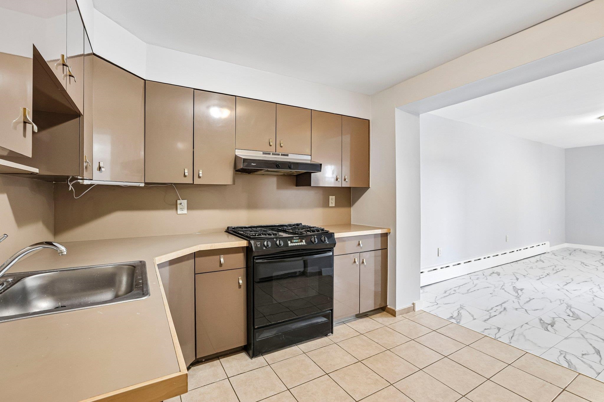 Kitchen with beige cabinets, a black gas range, and a sink beside an open unfurnished room.