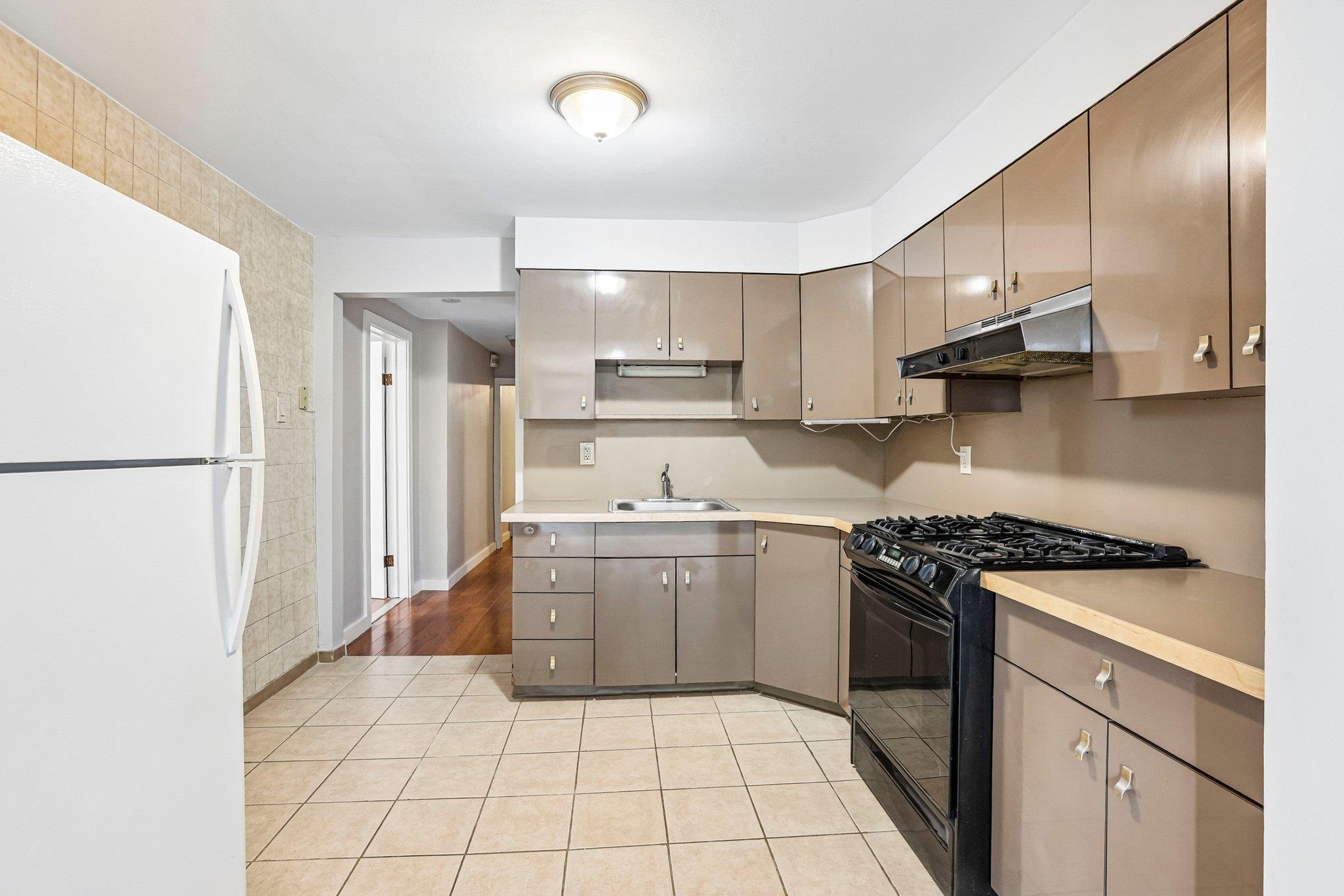Kitchen with beige cabinets, tiled floor, white refrigerator, and black gas range.