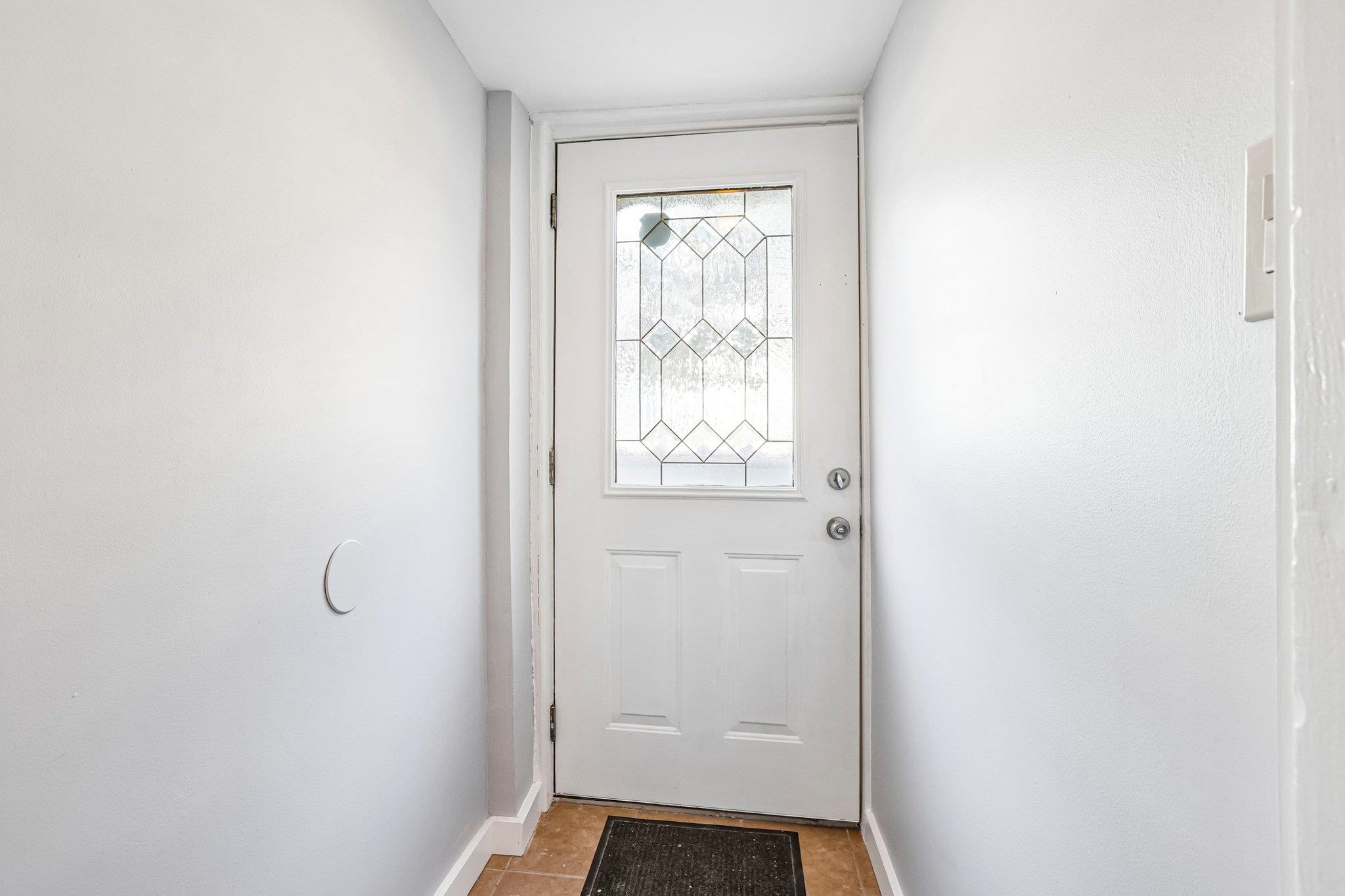 Entryway with a white front door featuring a decorative geometric glass panel and tan tile floor.