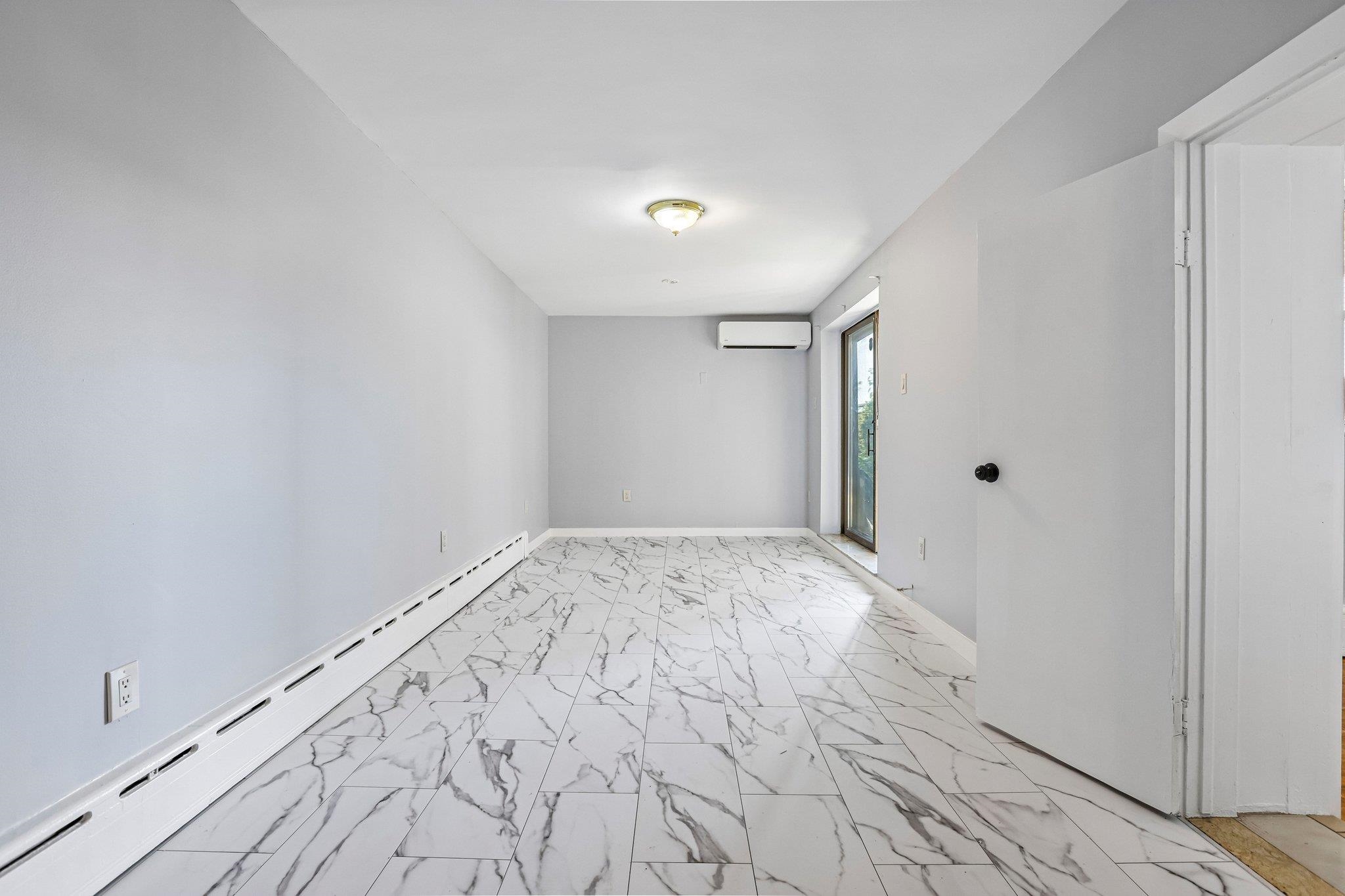 Empty room with marble-look tile floors, a wall-mounted mini-split, and a sliding glass door.